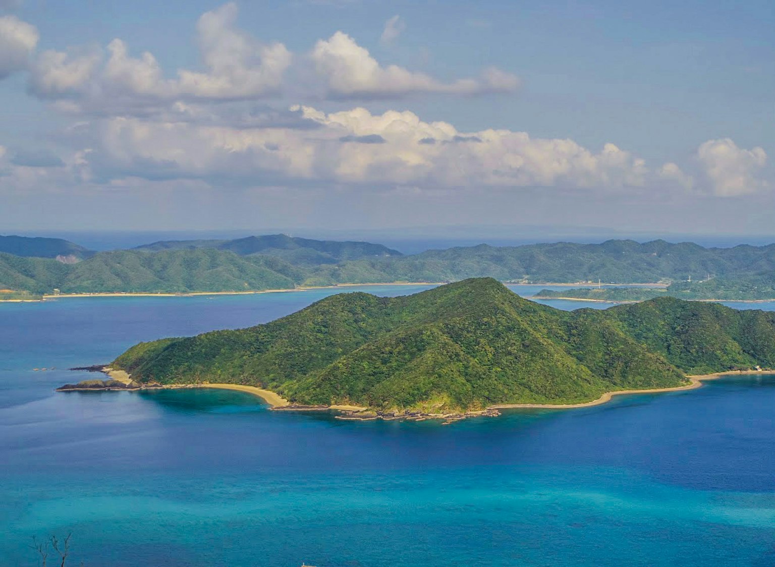 Luftaufnahme einer Insel mit grünem Hügel umgeben von blauem Wasser
