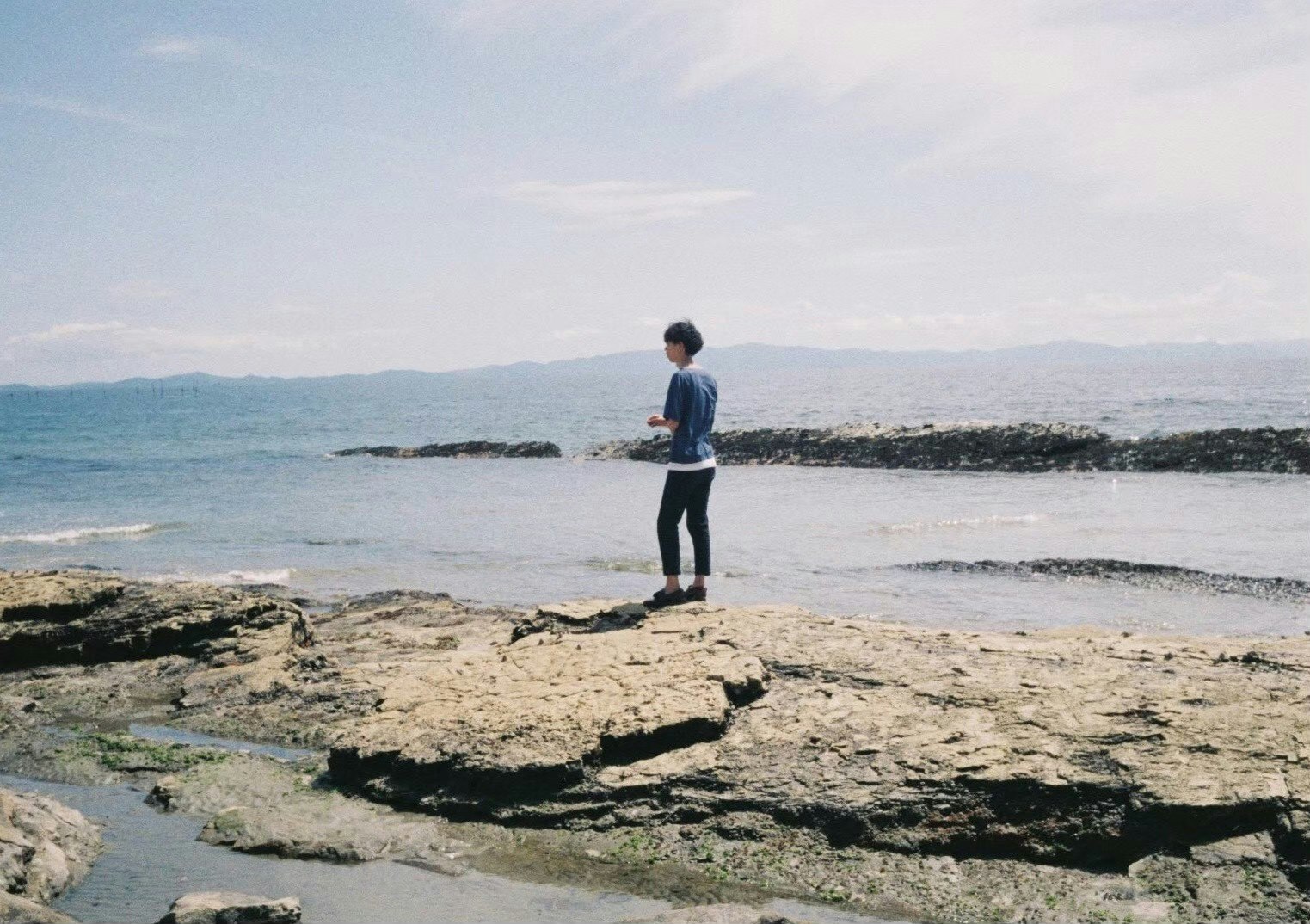 person standing on rocky shoreline overlooking the sea