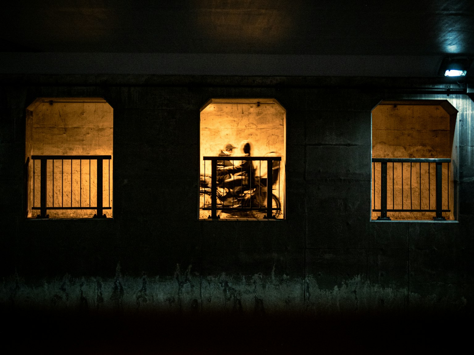 暗い背景に明るい窓があり、窓の中には人影と自転車が見える