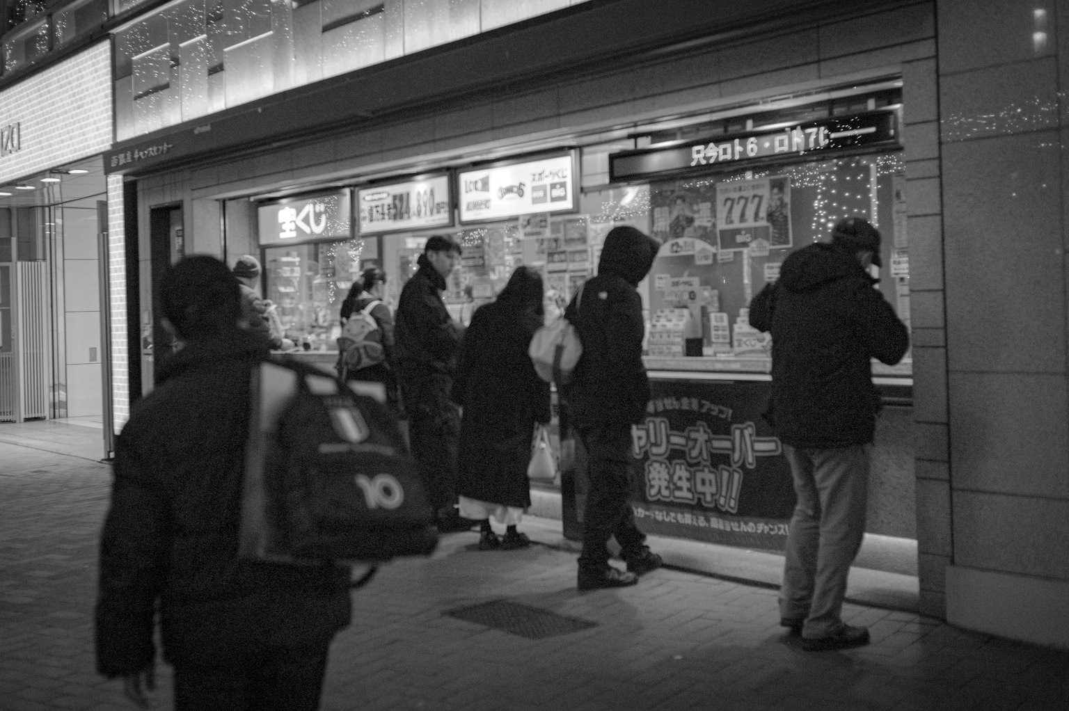 Scène en noir et blanc de personnes regardant un menu devant un magasin la nuit