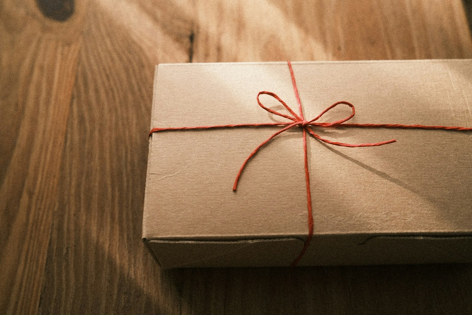 Una piccola scatola regalo avvolta in carta marrone legata con uno spago rosso su un tavolo di legno
