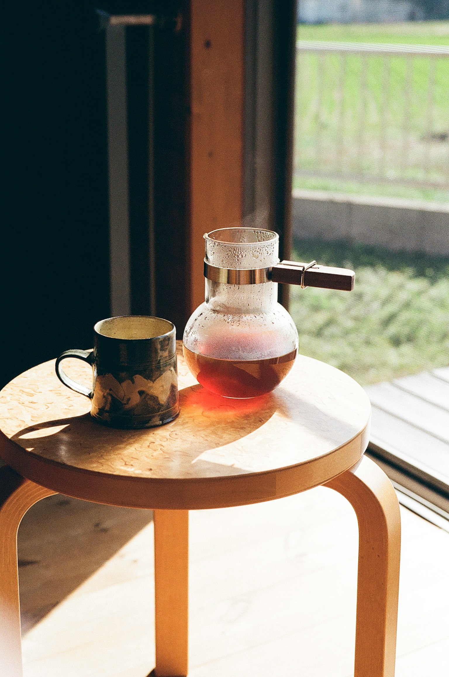木凳上的咖啡壺和杯子靠近陽光透射的窗戶