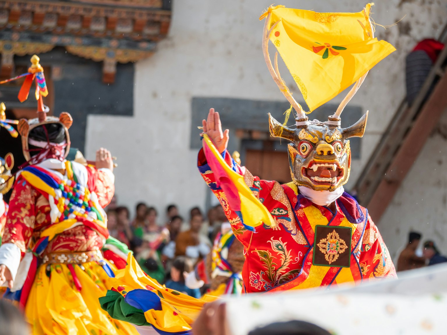 Danzatori in costumi colorati che indossano maschere tradizionali alzando le mani in una scena di festival