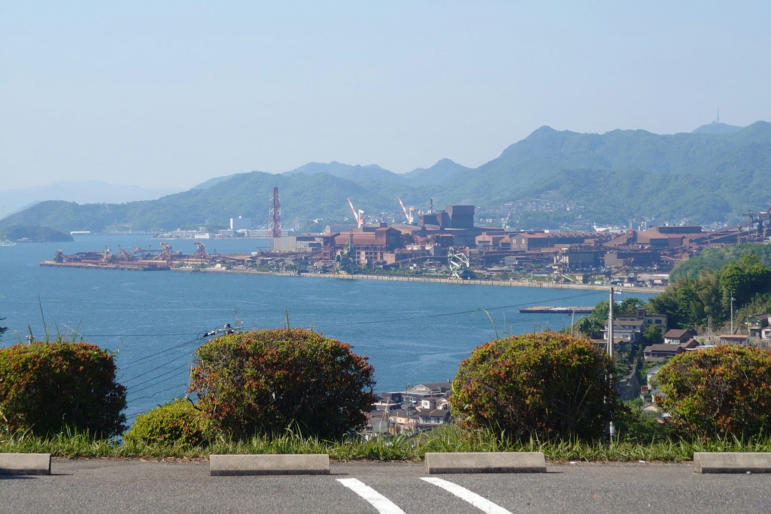 Scenic view of blue ocean and mountains with industrial buildings