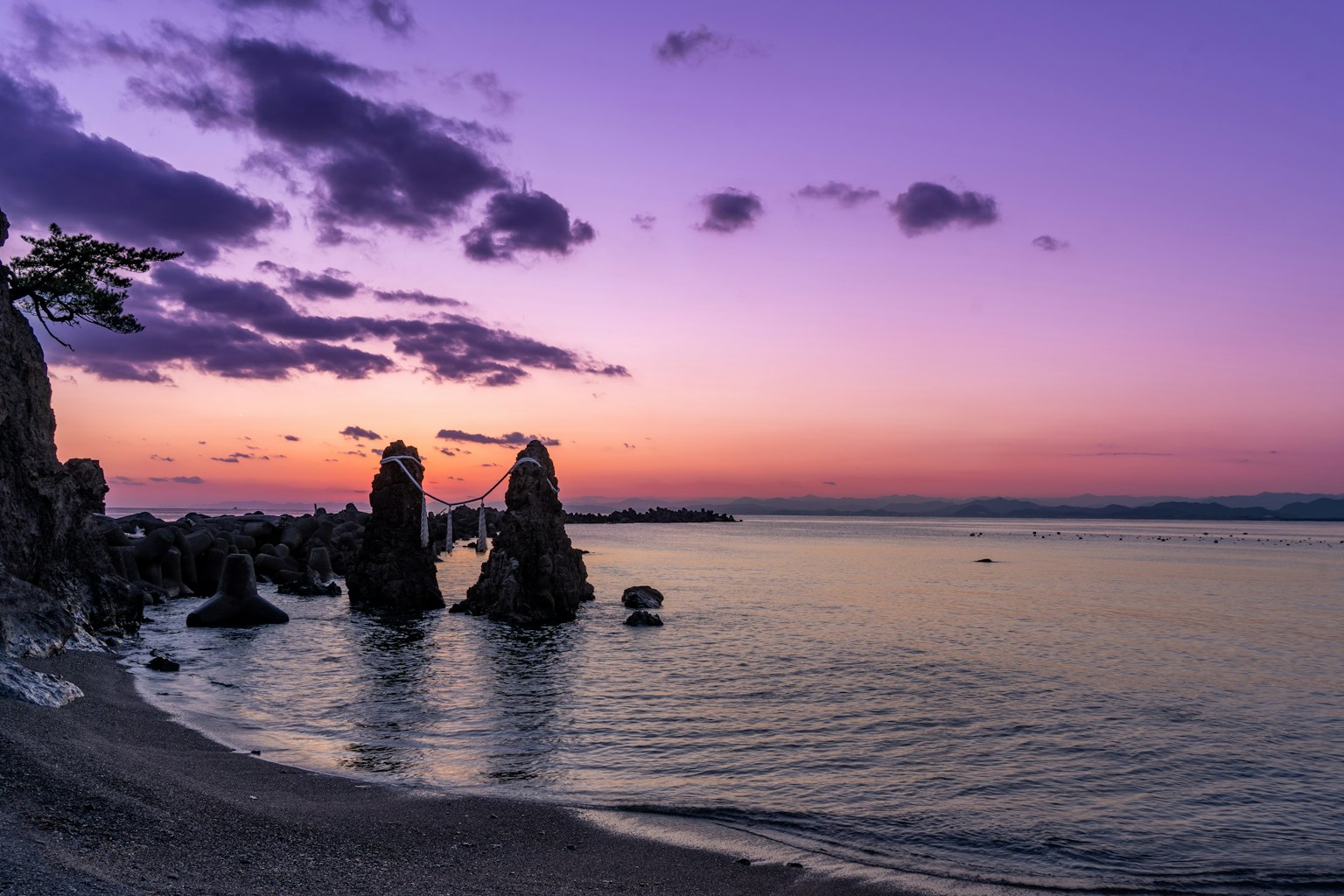 Rocas de pie en un mar tranquilo bajo un cielo púrpura al atardecer