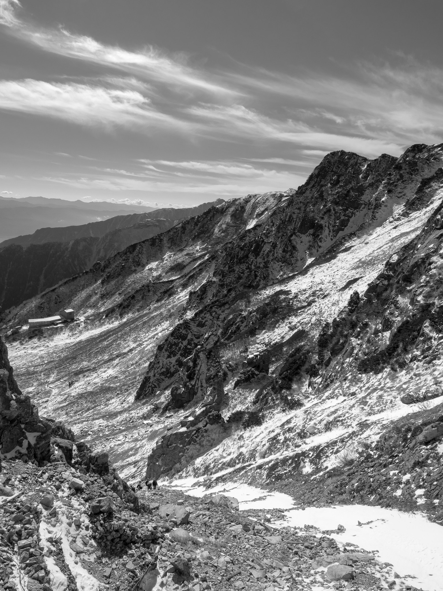 Black and white mountain landscape with steep cliffs and rocky layers distant mountains and clouds