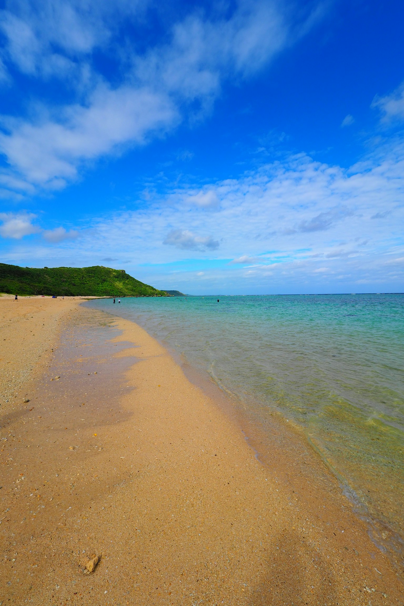 Beach landscape with blue sky and ocean sand shore and green hill visible