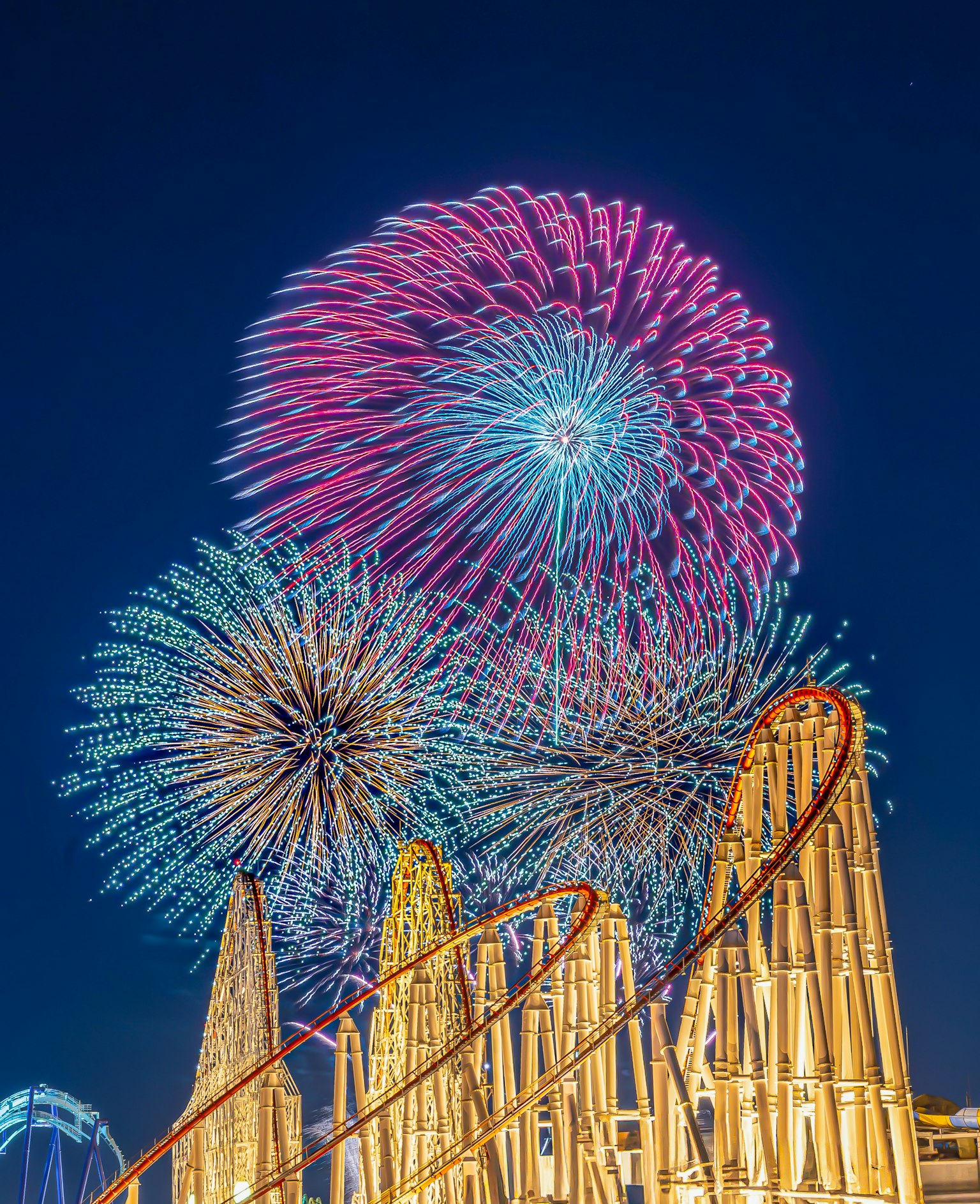 Fuegos artificiales coloridos estallando en el cielo nocturno sobre una montaña rusa
