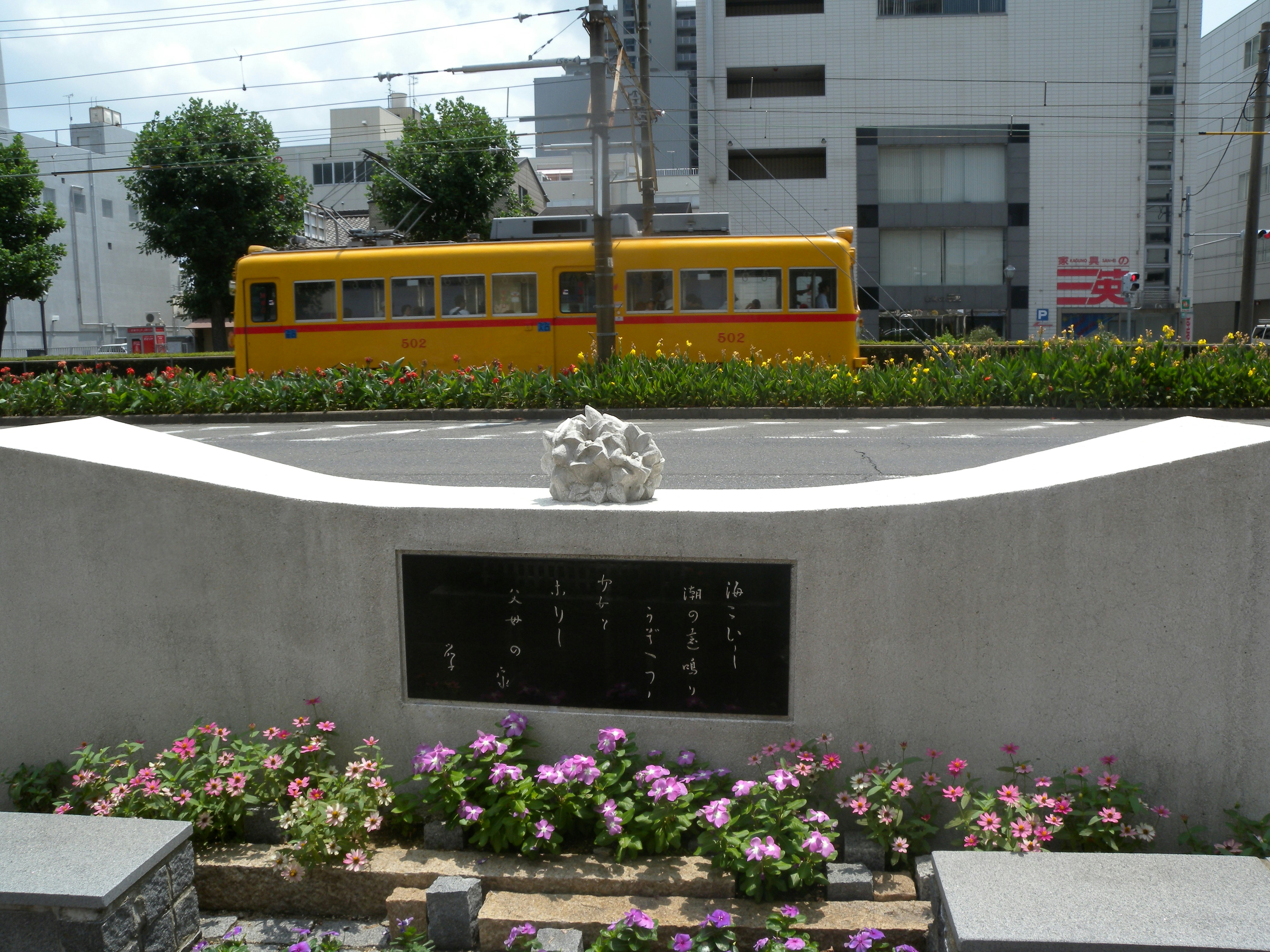 黄色い路面電車と花壇のある都市のモニュメント
