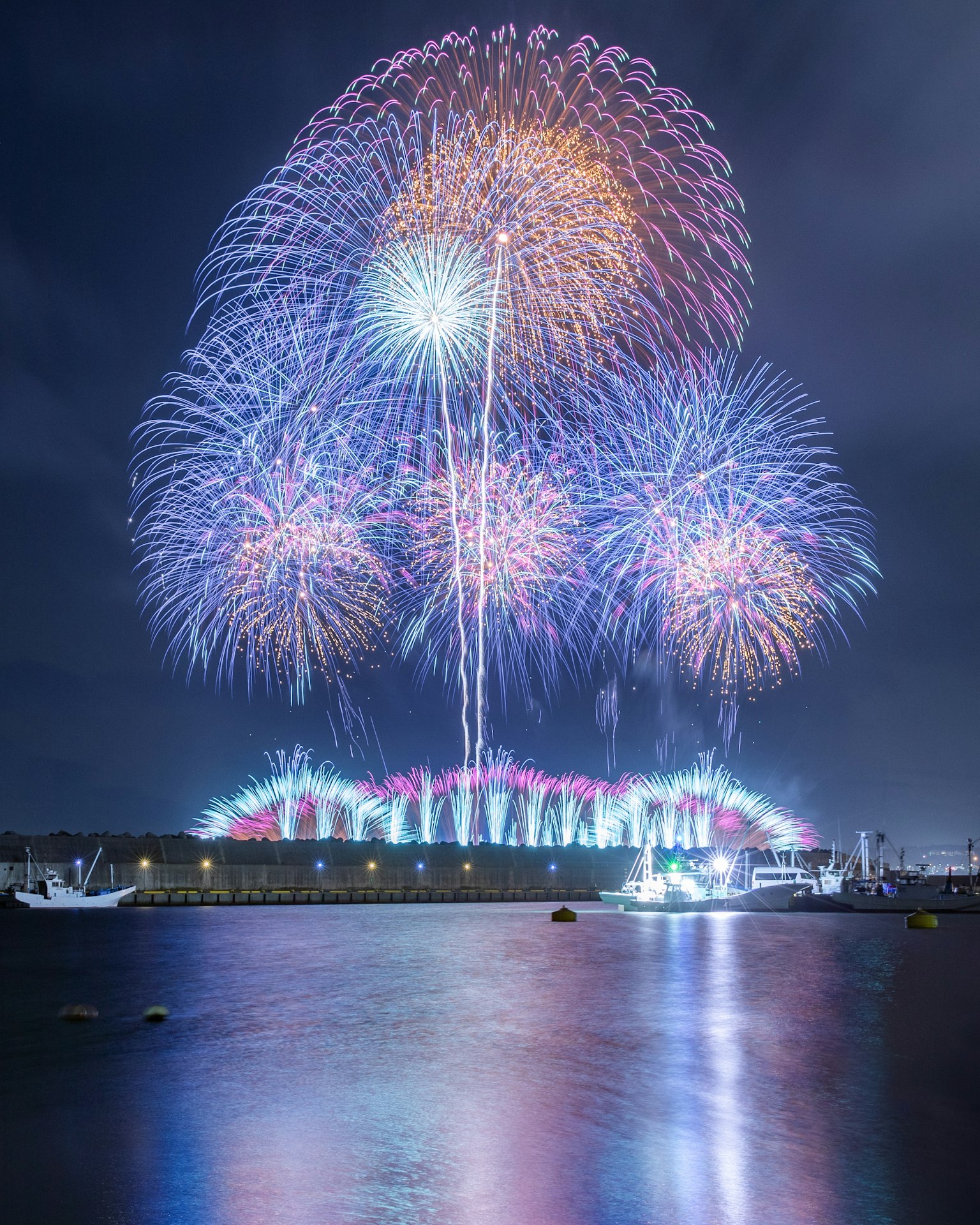 Fuegos artificiales coloridos iluminan el cielo nocturno reflejándose en el agua