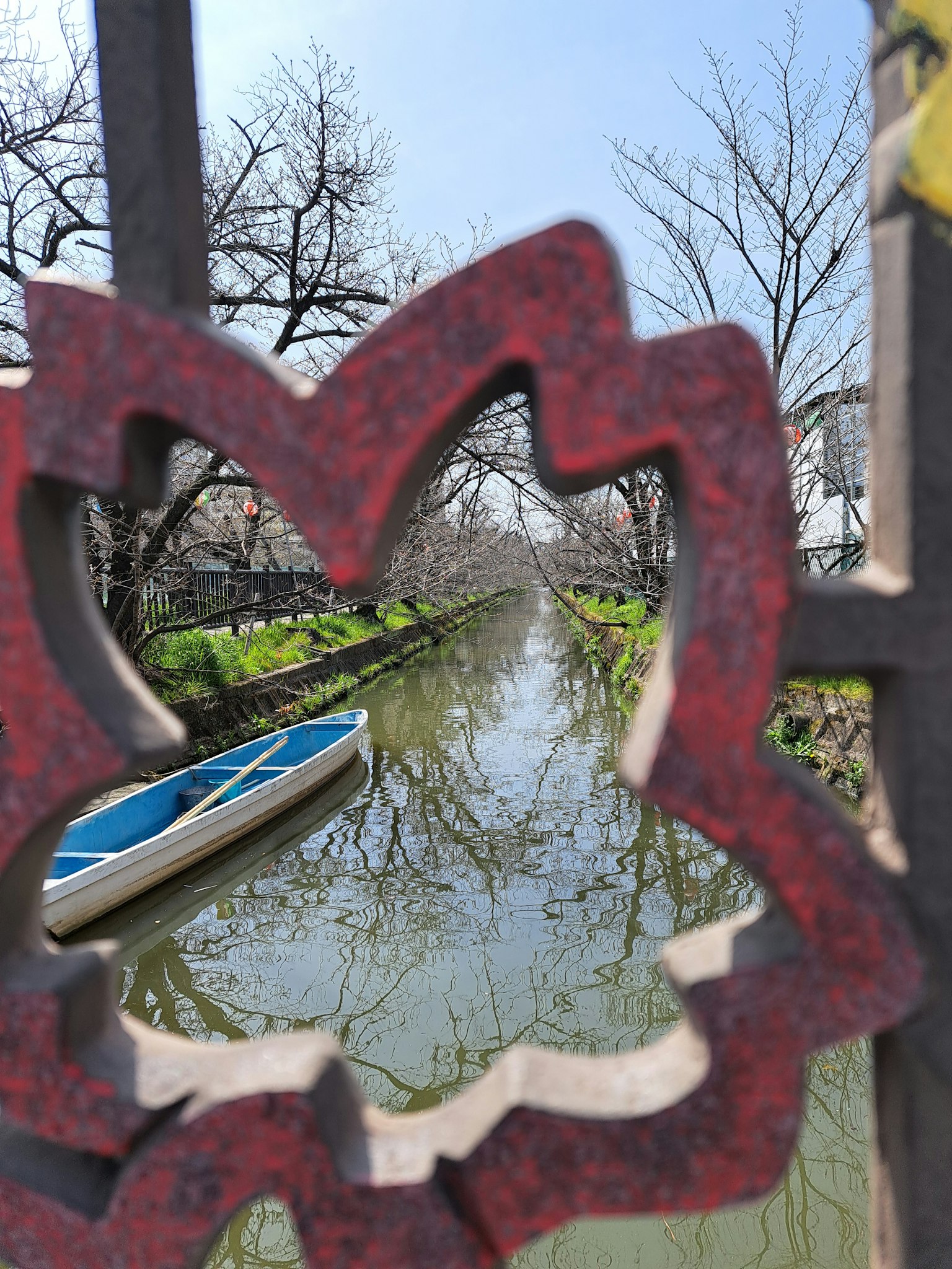 View through a red flower-shaped fence revealing a tranquil canal and a boat