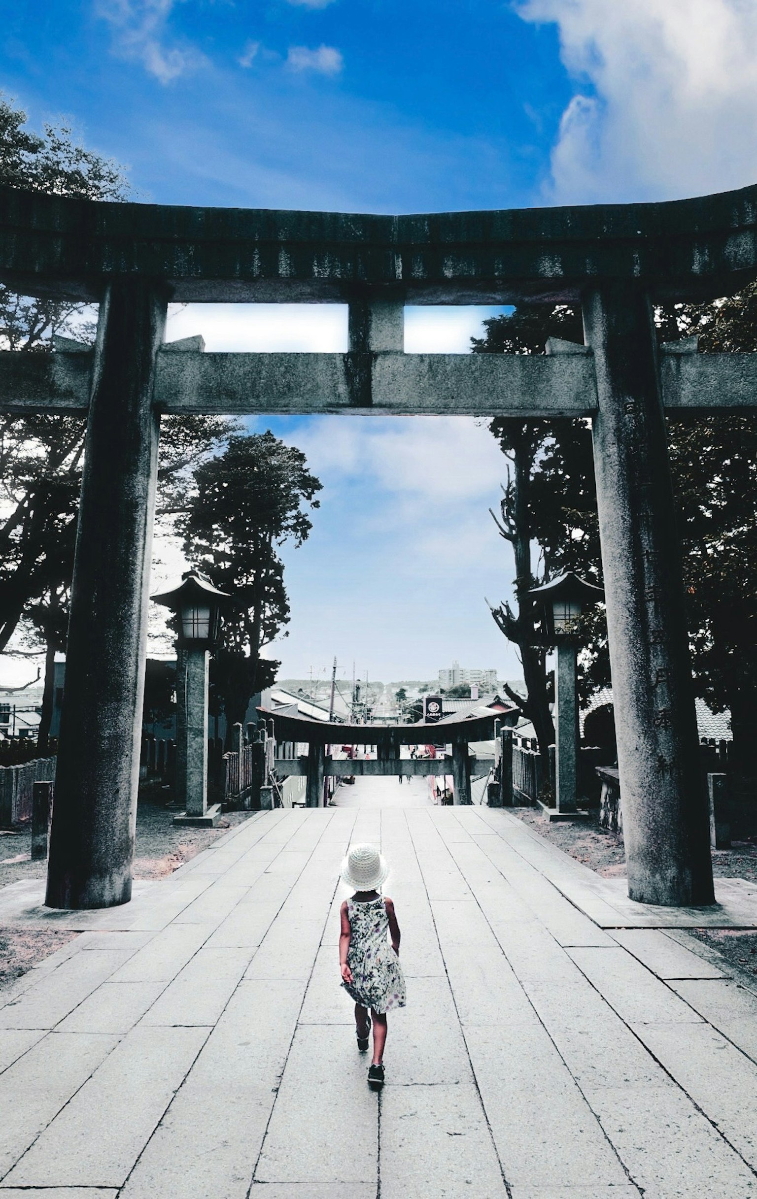 Un bambino che cammina sotto un torii con cielo blu e alberi verdi