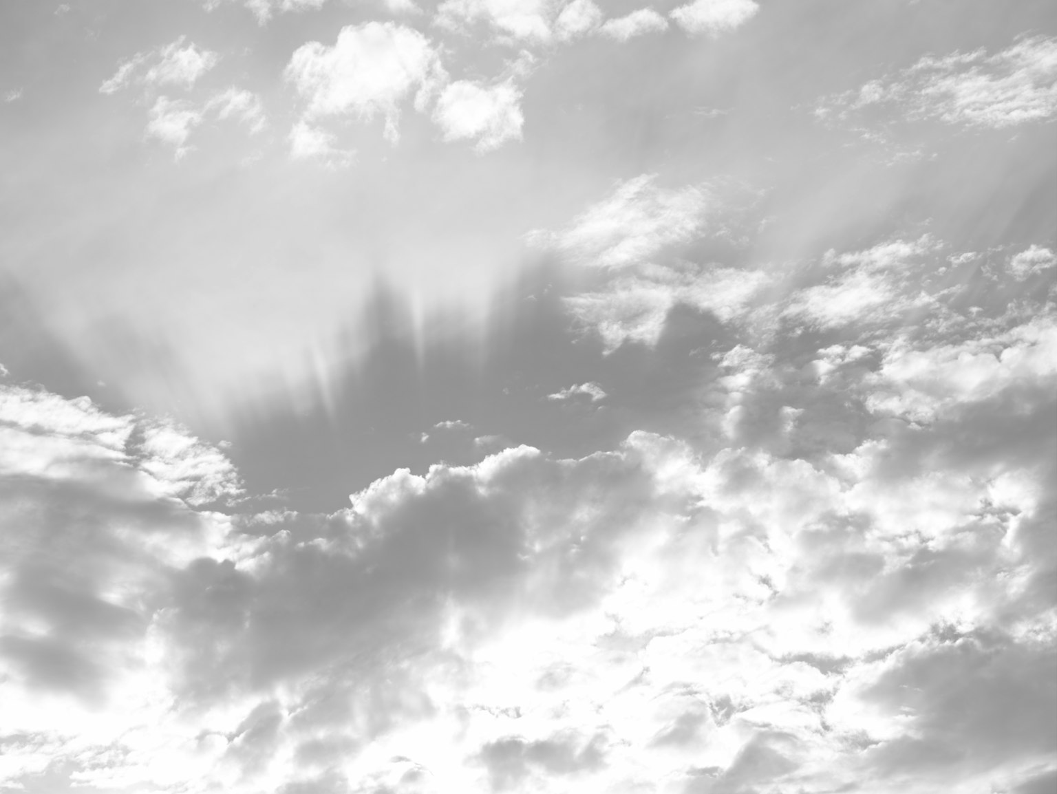 Black and white image of clouds with rays of light breaking through