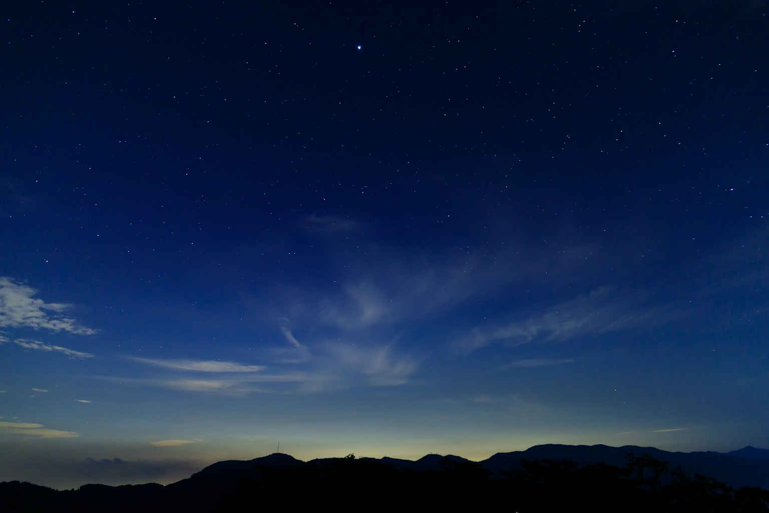 Eine schöne Landschaft mit im Nachthimmel leuchtenden Sternen, silhouettiert von niedrigen Bergen