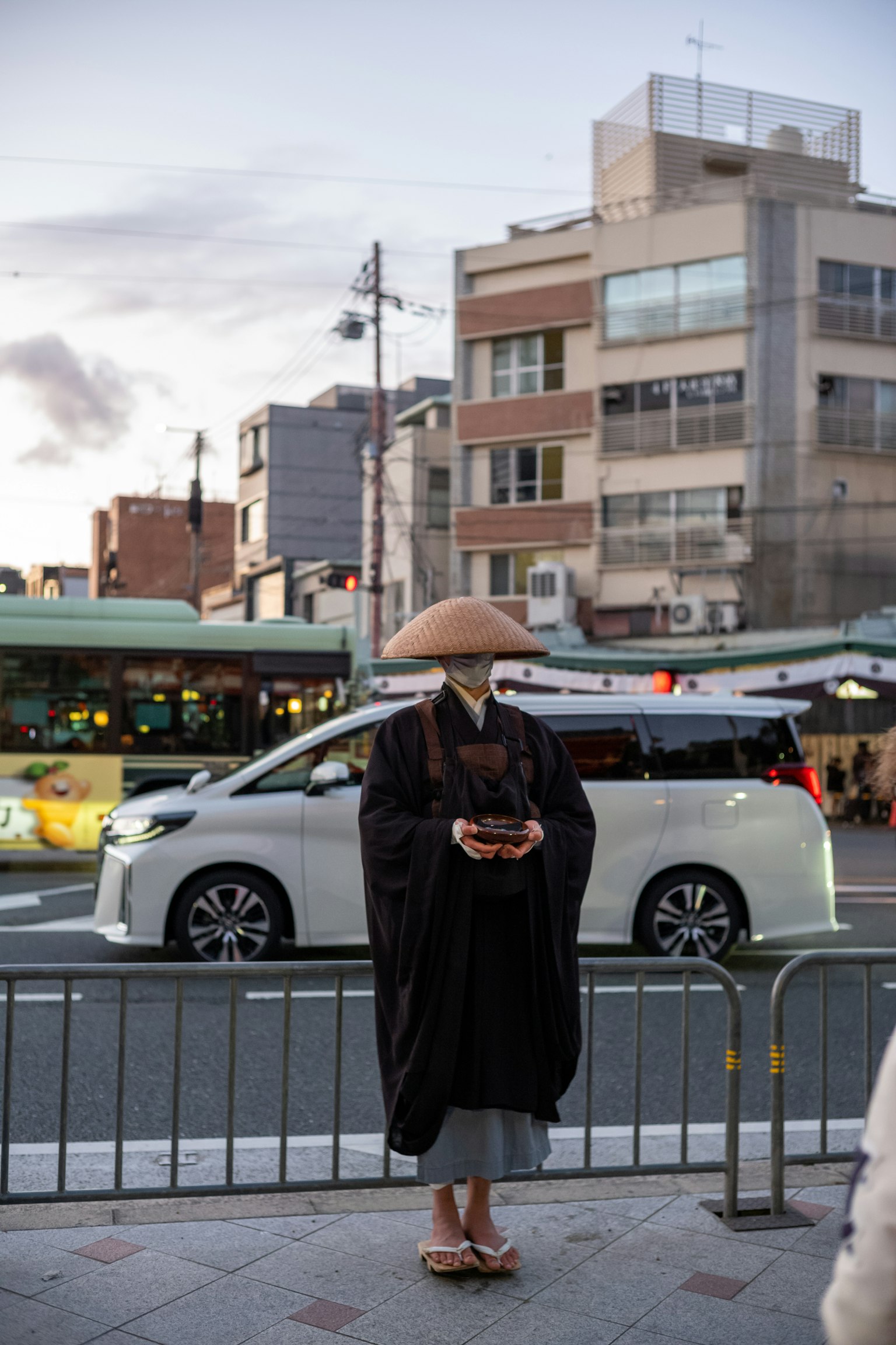 一位穿著傳統服裝的人站在街角，背景中有一輛車經過