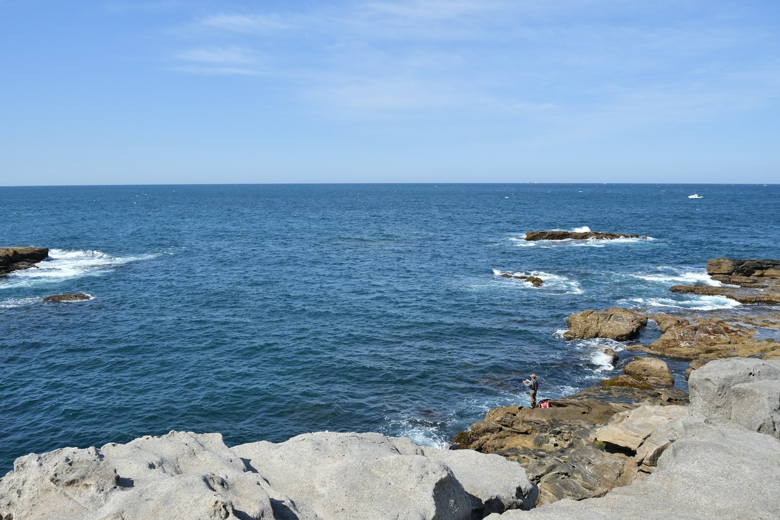 Un pêcheur sur une côte rocheuse avec un océan bleu et un ciel dégagé
