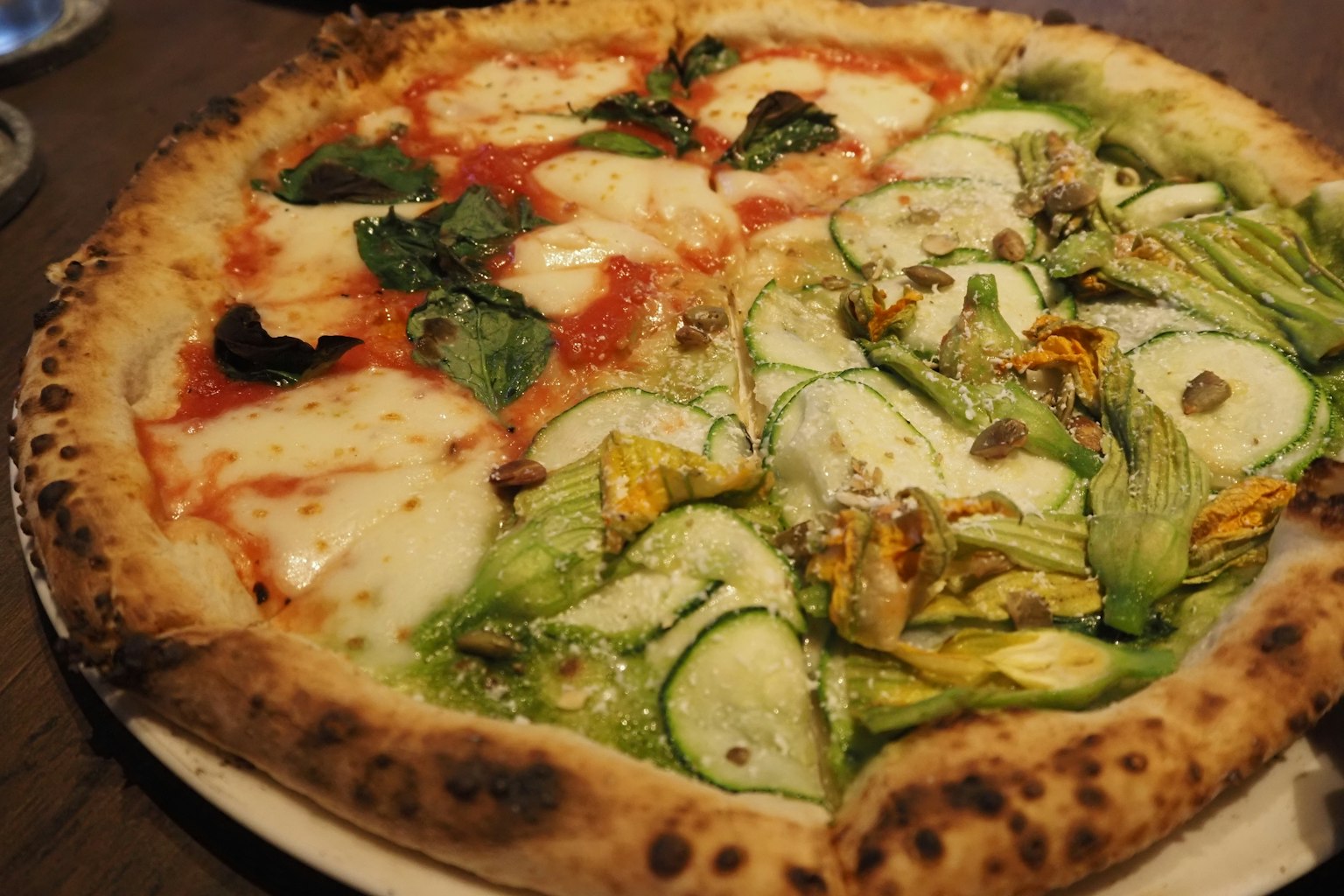 Pizza mitad salsa de tomate y mozzarella con albahaca y mitad pizza con calabacín y flores
