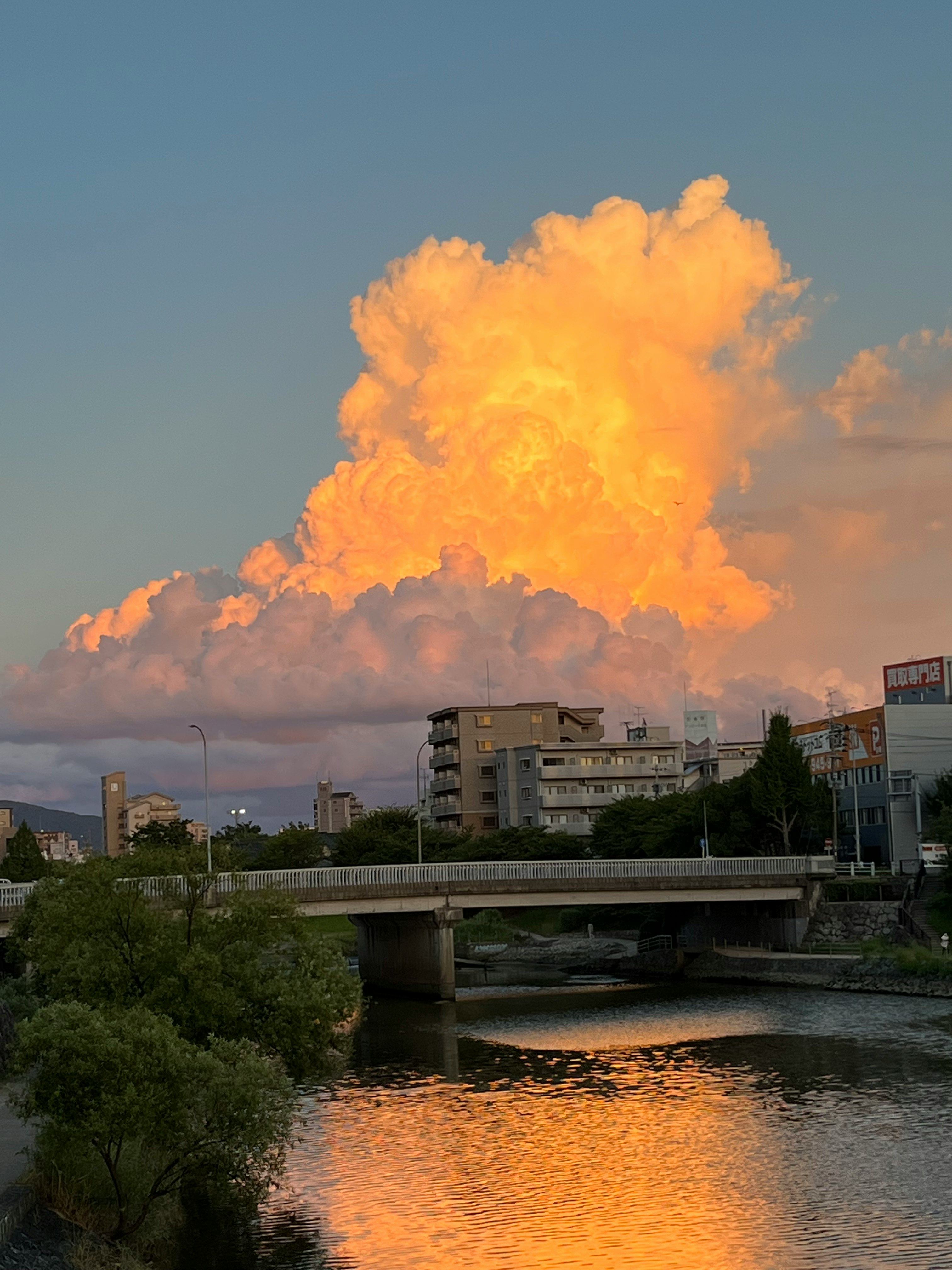 夏の夕空に広がる入道雲と川沿いの橋の風景
