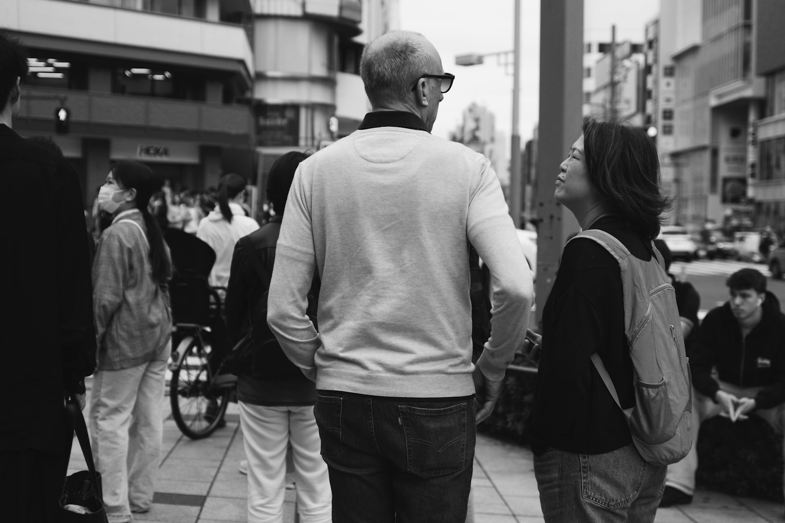 도시의 번화한 거리에서 보행자들에 둘러싸여 대화하는 두 사람
