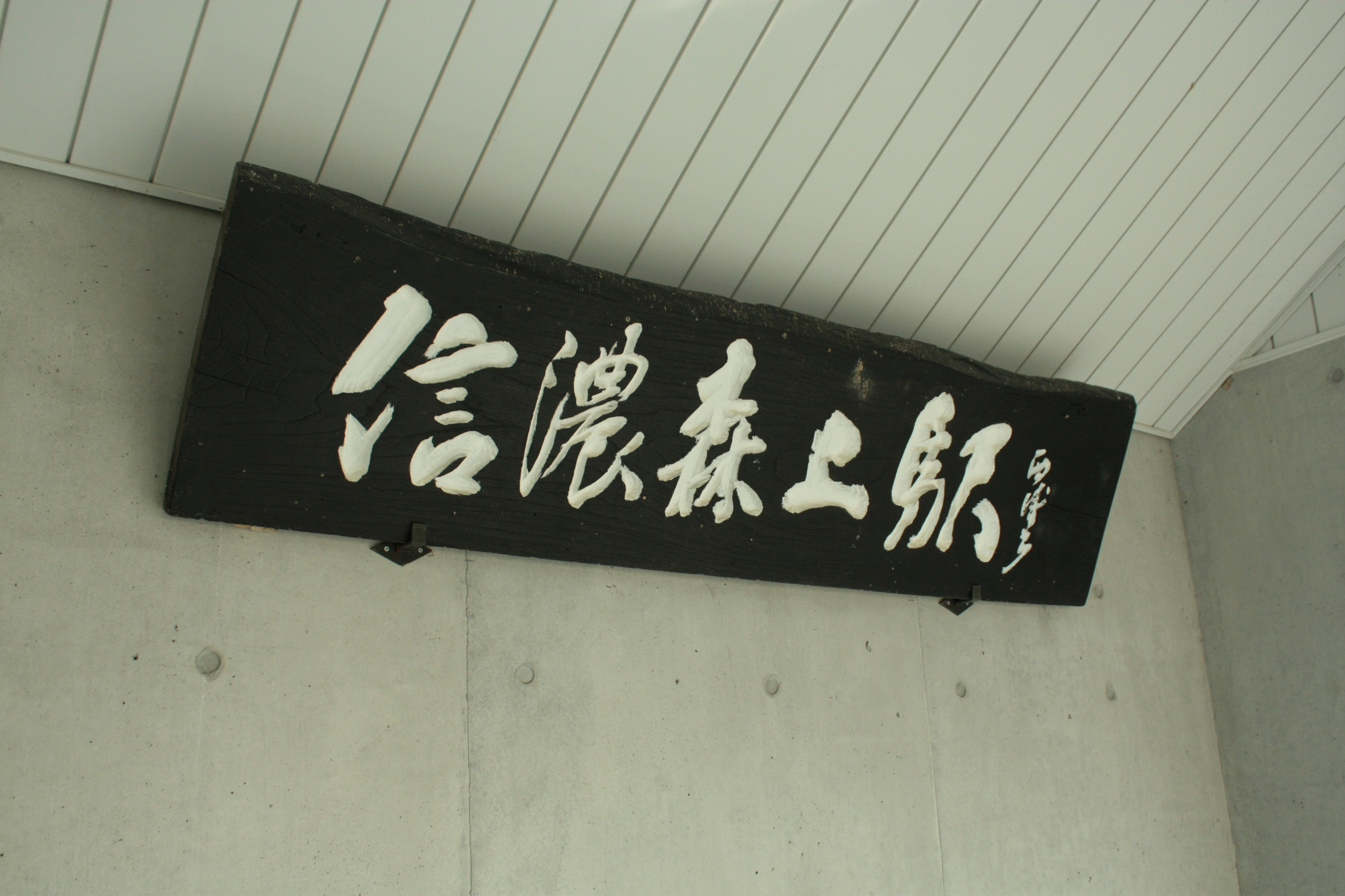 schwarzes Ladenschild mit weißen Schriftzeichen unter einem Vordach