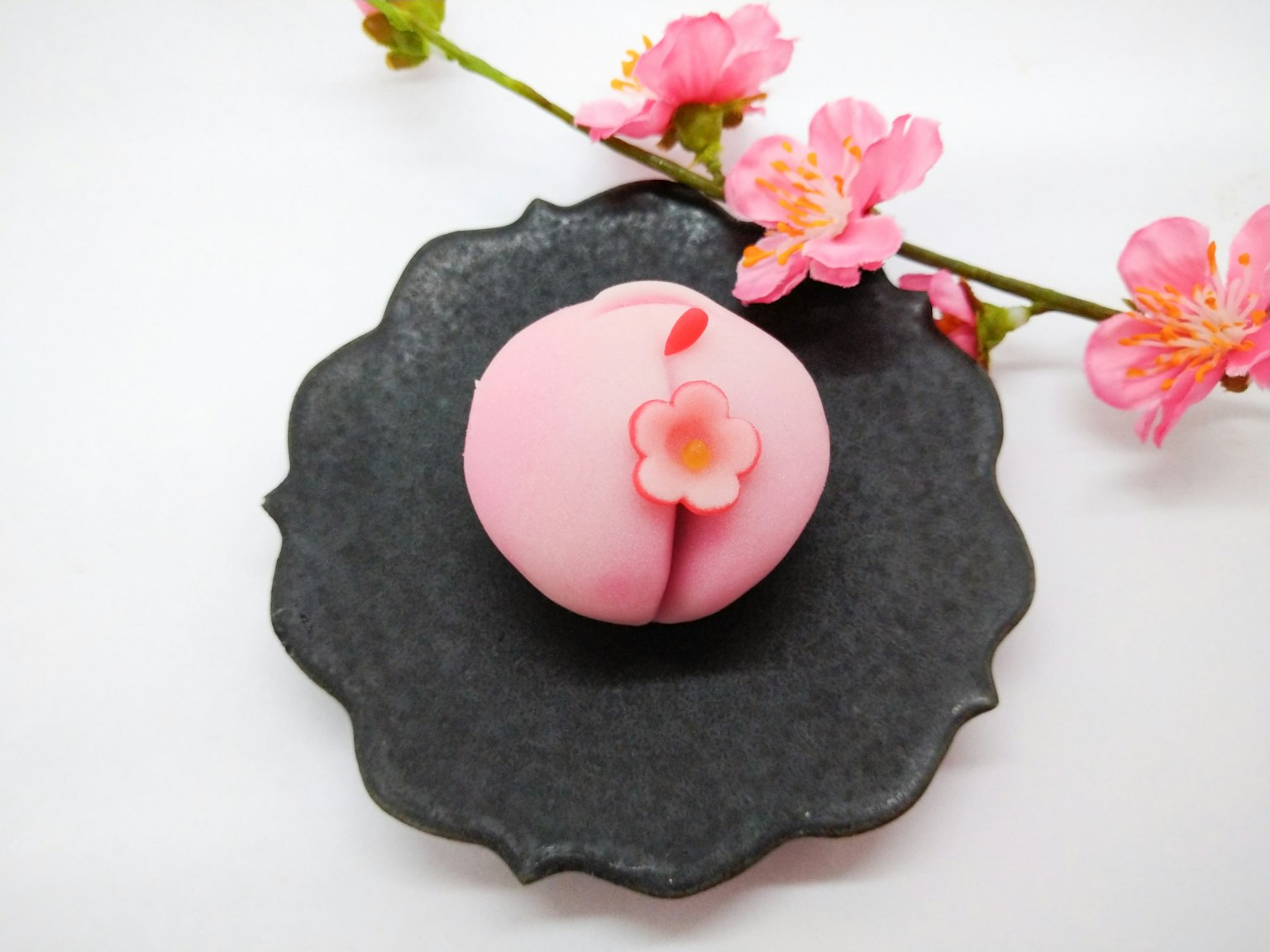 Confitería japonesa rosa en un plato negro con decoración floral