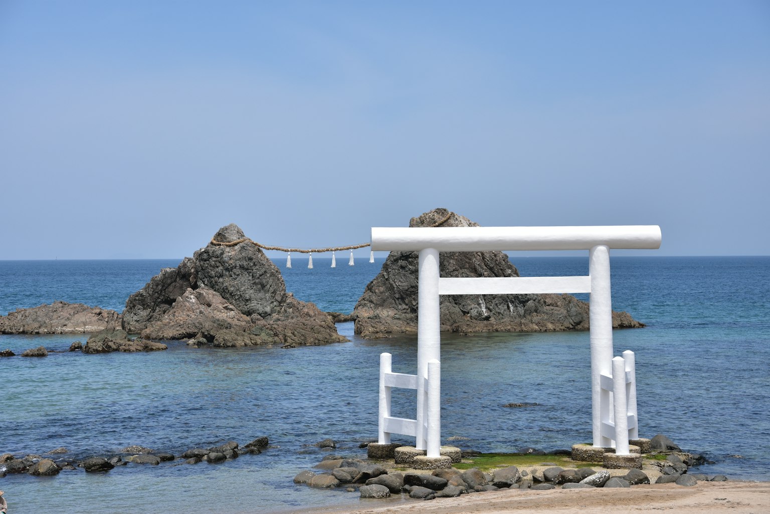 Cổng torii trắng với cảnh biển và các hòn đảo đá