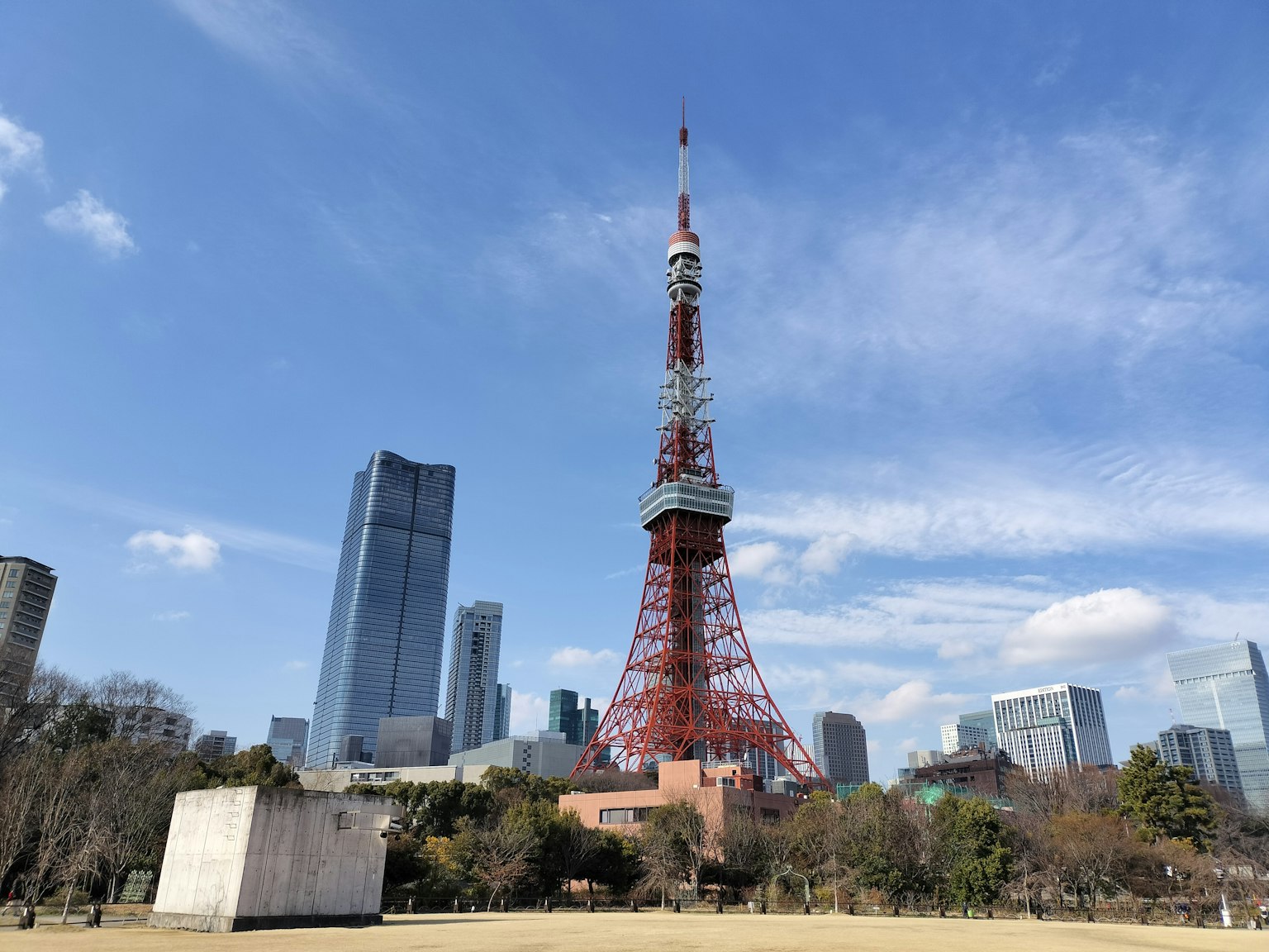 Menara Tokyo dikelilingi gedung pencakar langit modern di bawah langit biru dengan awan putih