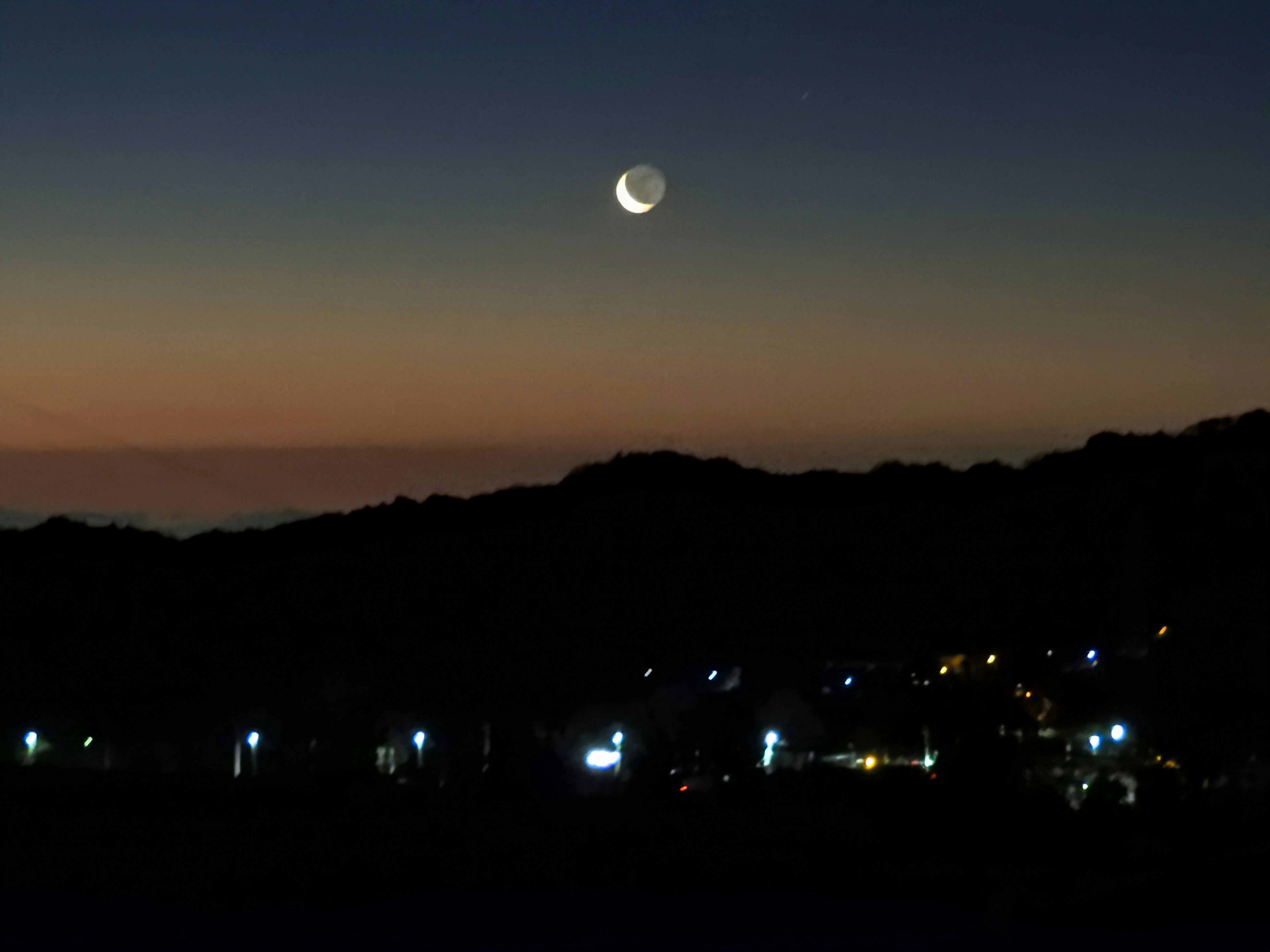 cielo antes del amanecer con la luna saliendo por el este sobre una silueta urbana