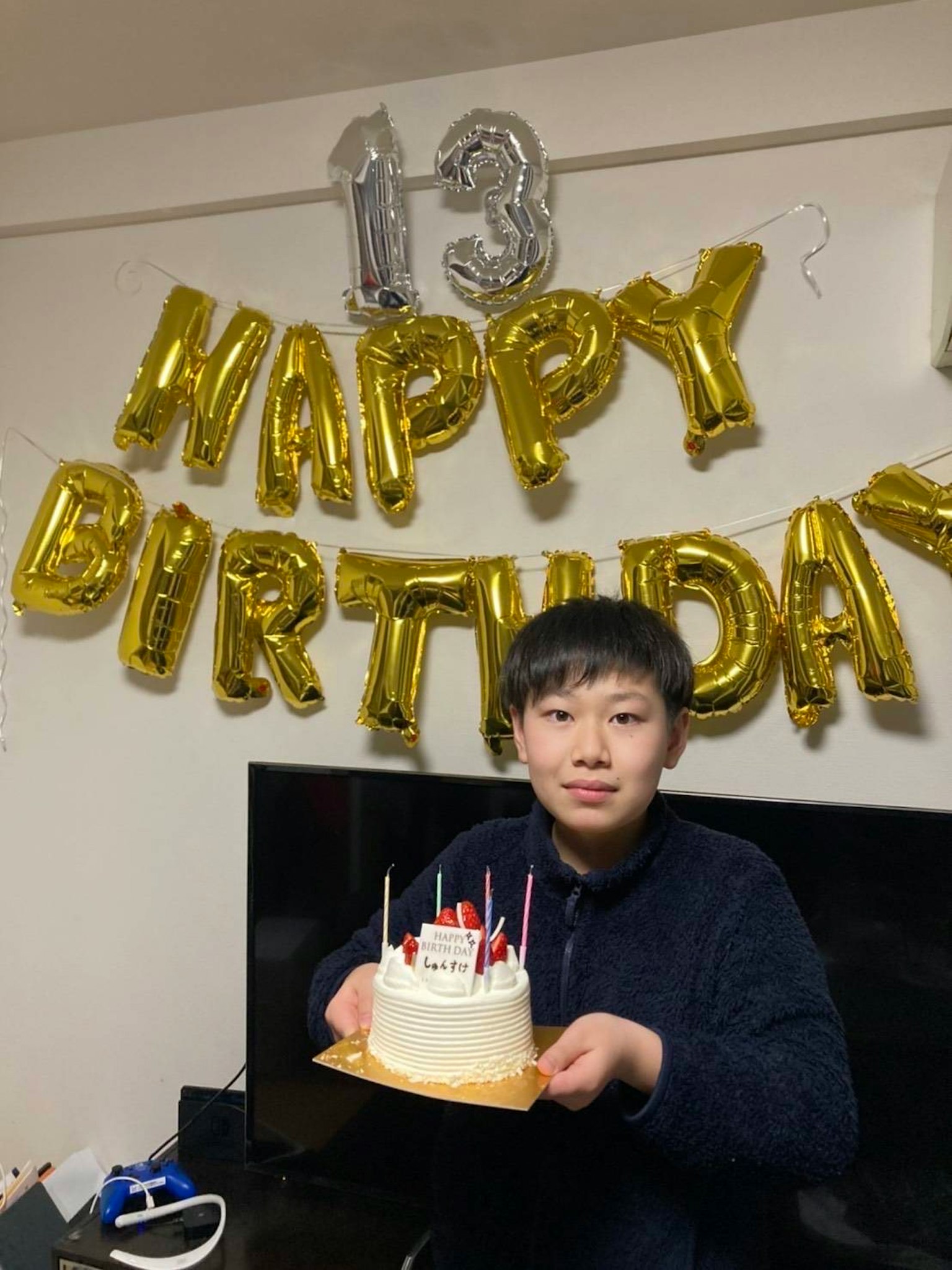 Ein Junge, der seinen 13. Geburtstag feiert und einen Kuchen in einem dekorierten Raum hält