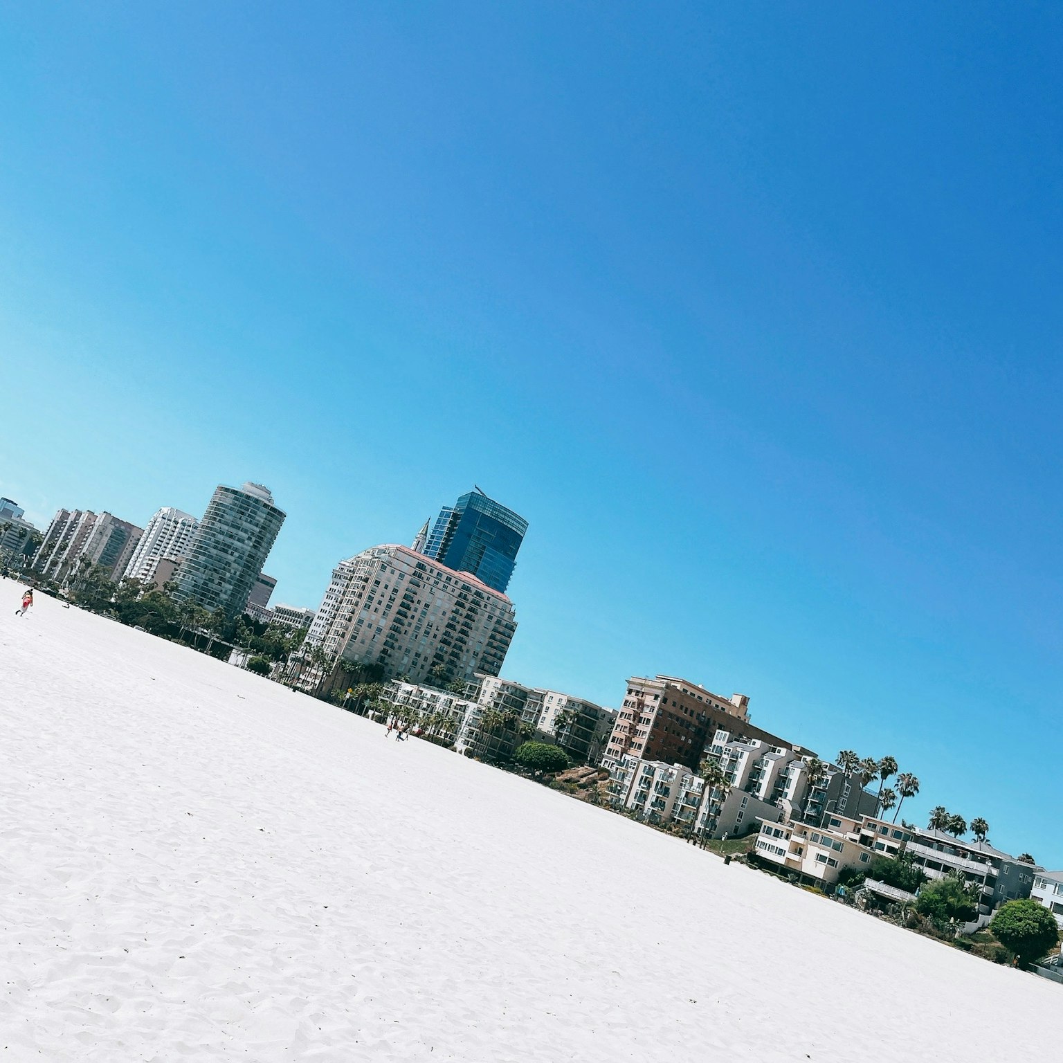 A view of a white sandy beach with tall buildings under a clear blue sky