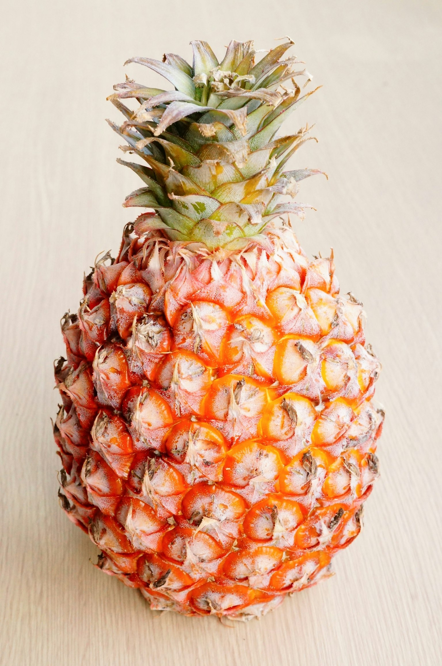 Una piña con tonos anaranjados colocada sobre una mesa de madera