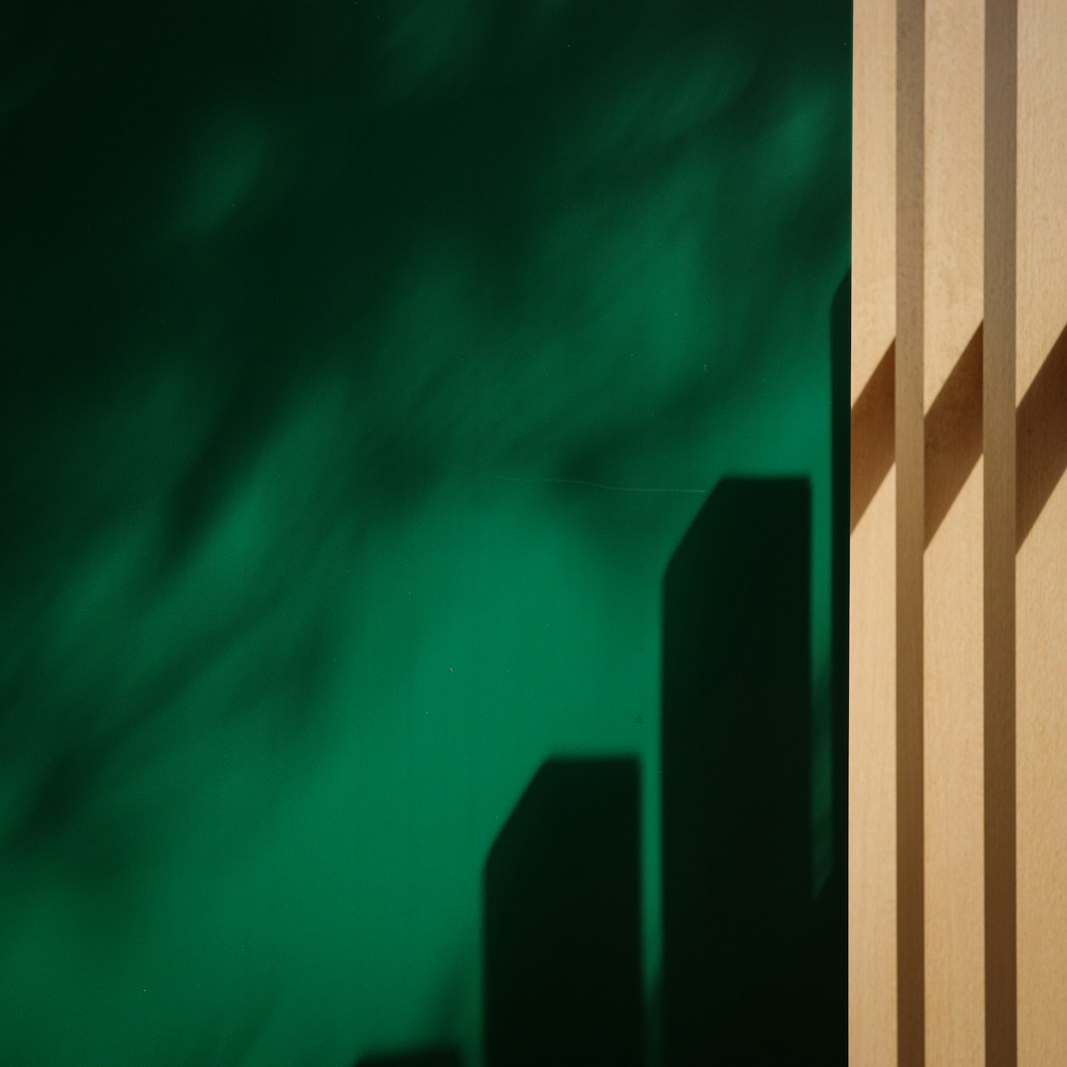 Simple composition with wooden pillars casting shadows on a green background