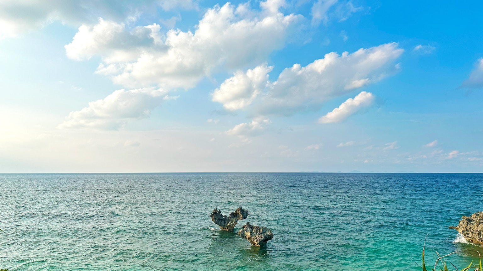Eine ruhige Aussicht auf den blauen Ozean und den Himmel mit Wolken und einem alten Boot, das schwimmt