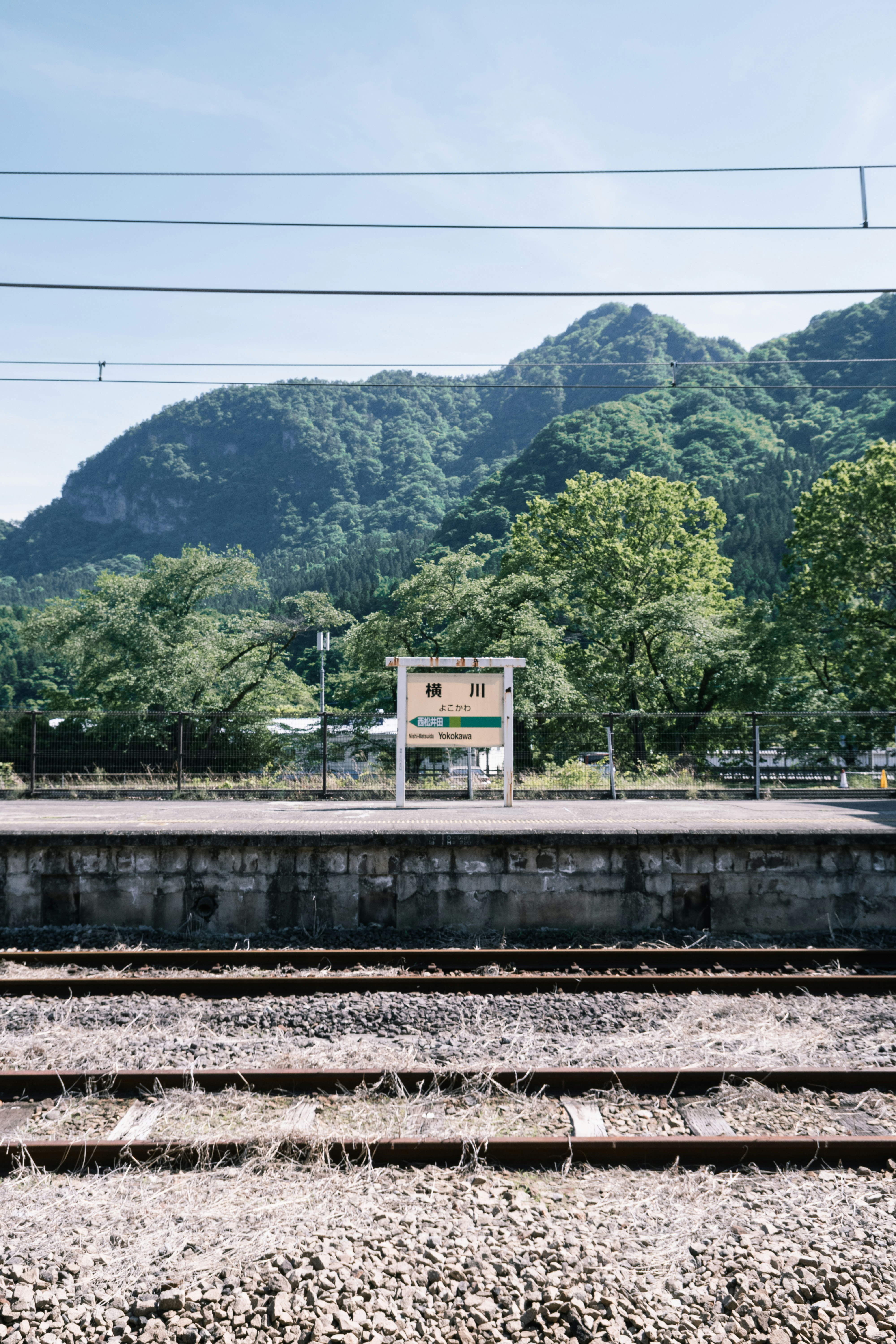 山並みを背景にした線路沿いの駅前看板のある風景