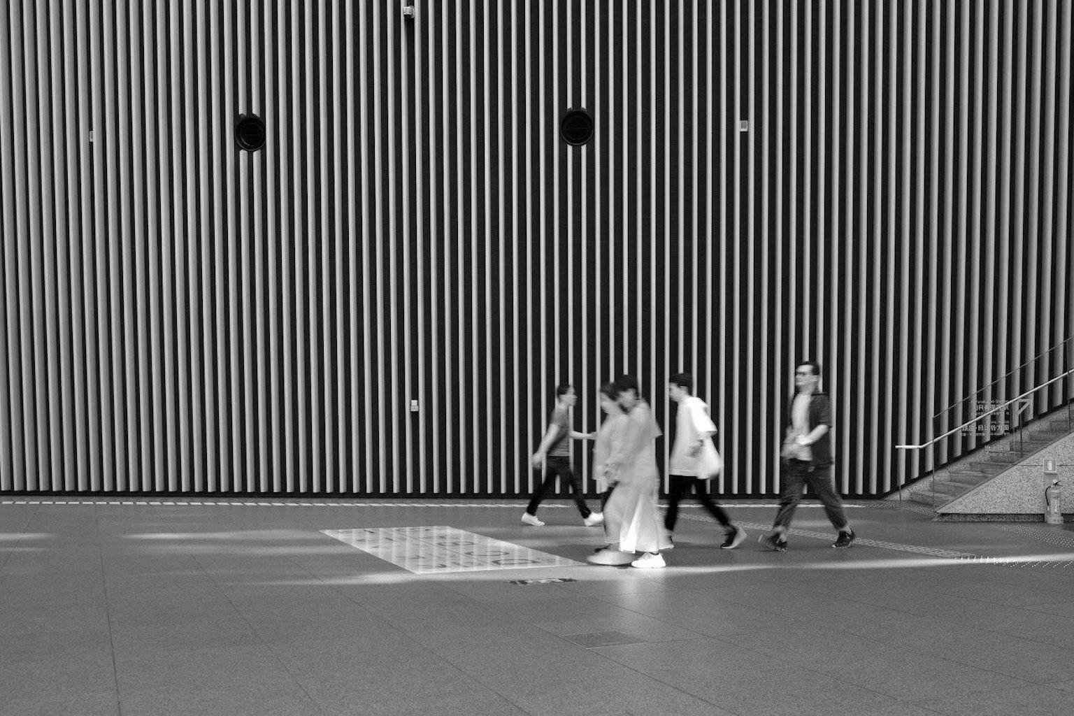 Gruppo di persone che camminano davanti a un muro a strisce bianche e nere