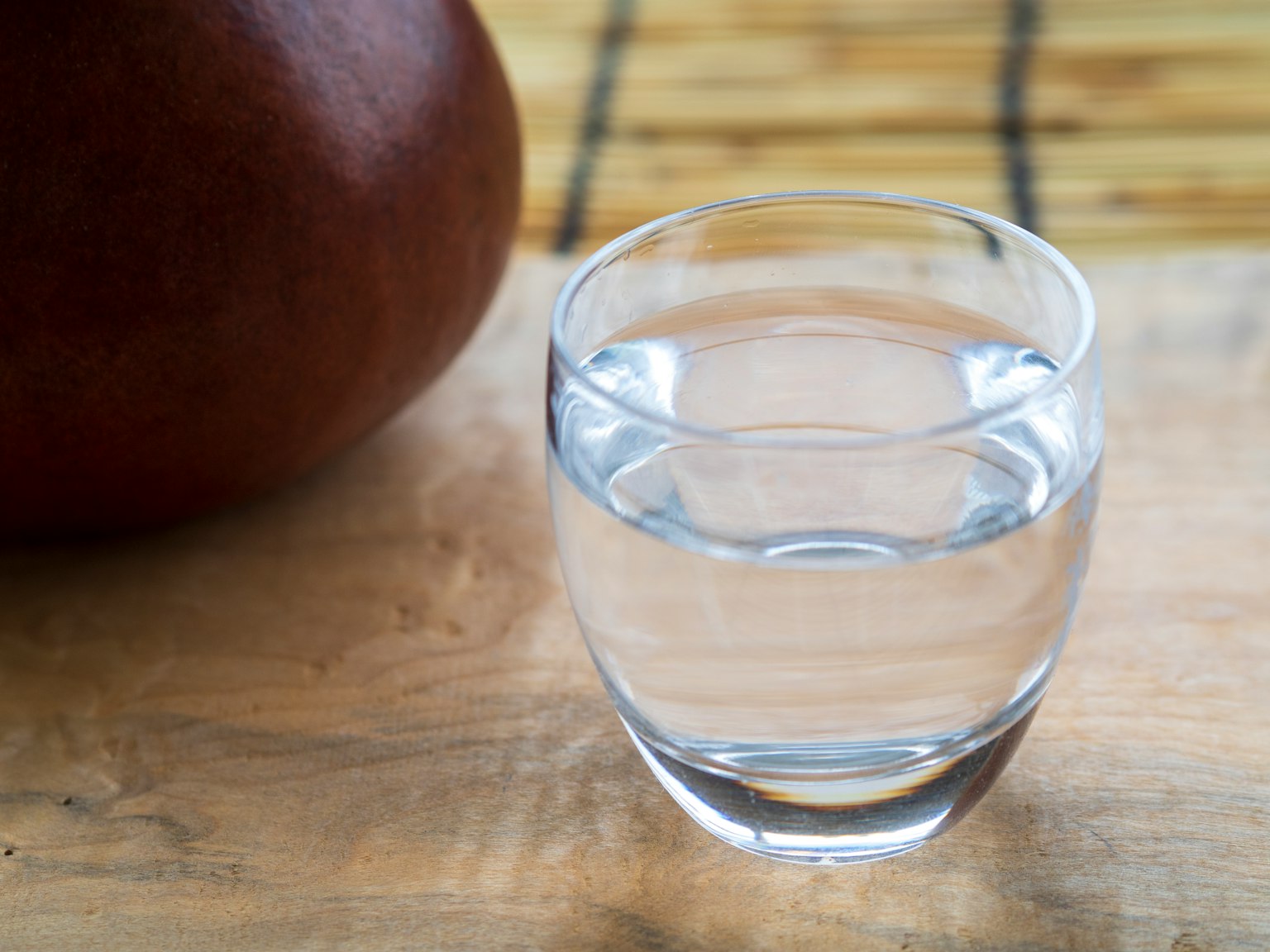 Un vaso de agua clara junto a una olla marrón sobre una mesa de madera