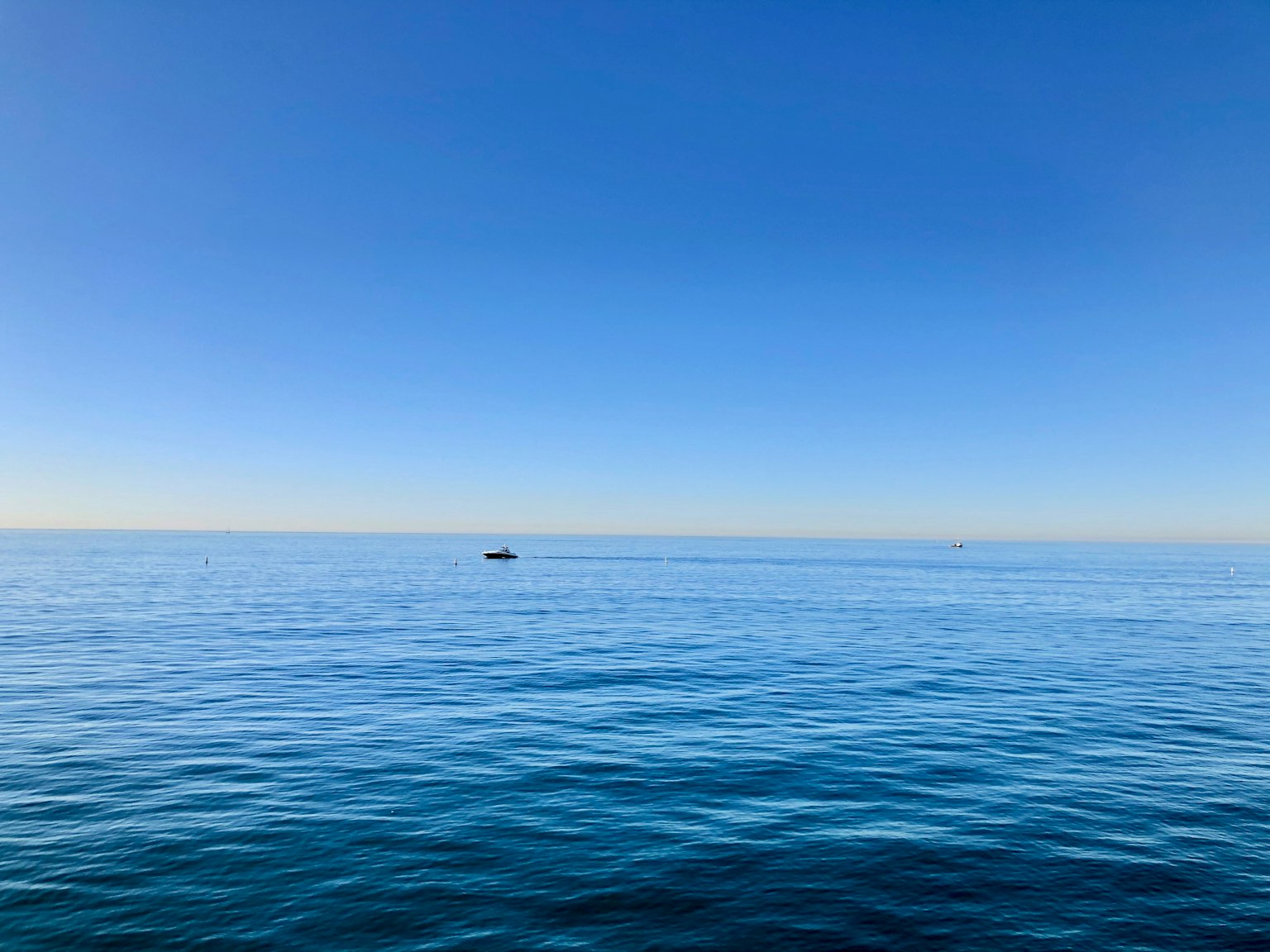 Pemandangan tenang laut dan langit biru dengan perahu kecil di kejauhan