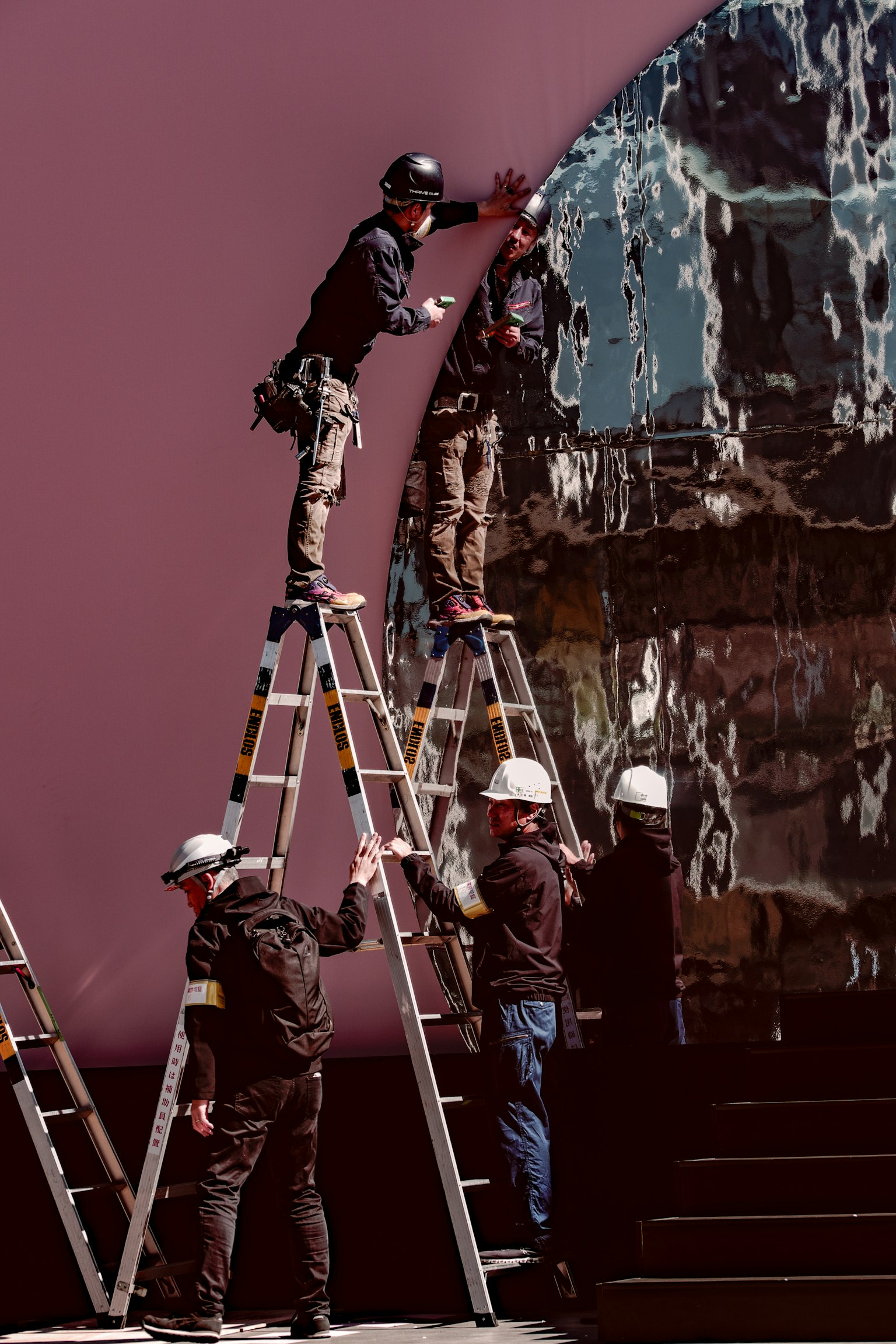 Lavoratori che regolano un grande pannello metallico usando scale