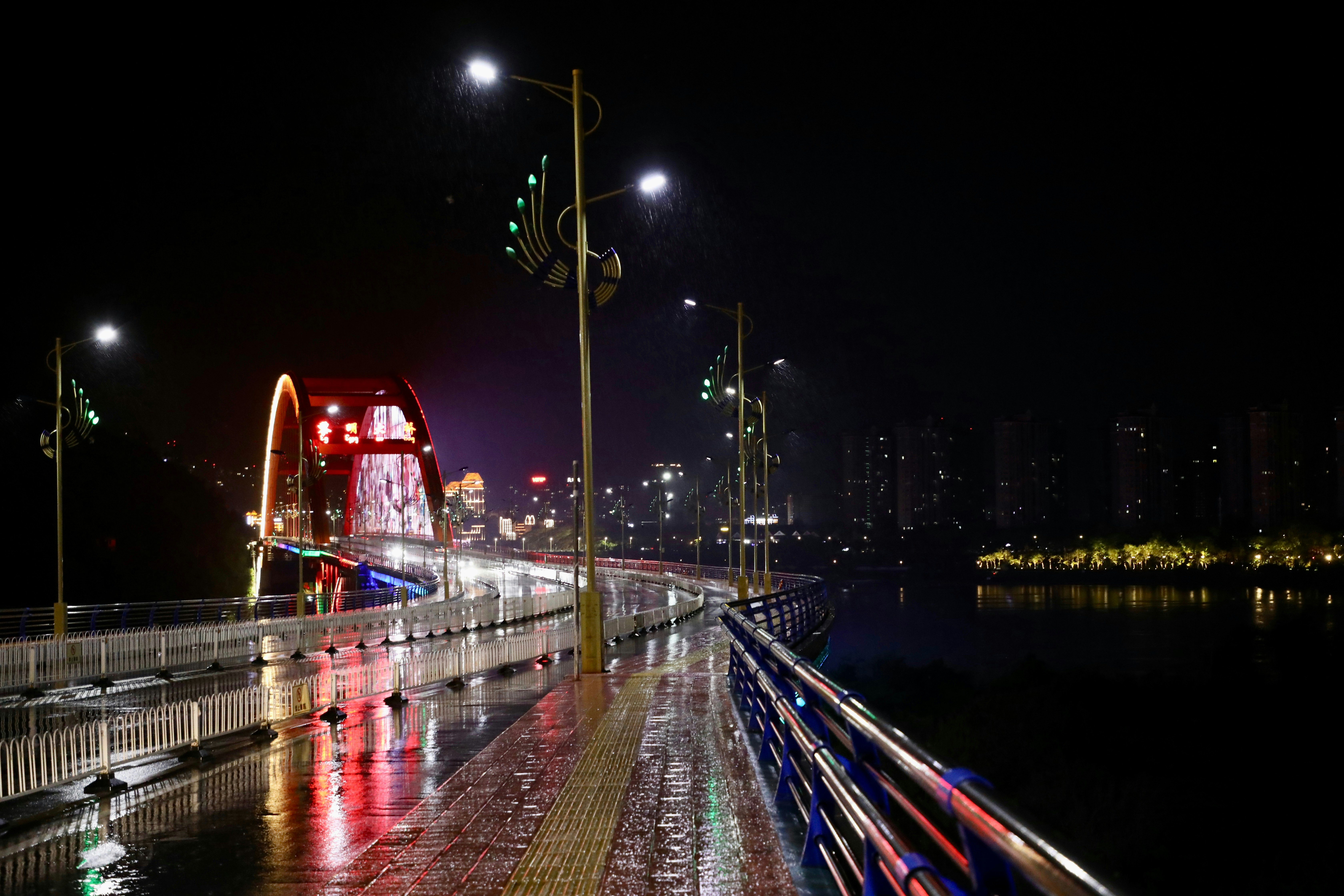 夜の川沿いの遊歩道とライトアップされた橋の眺め
