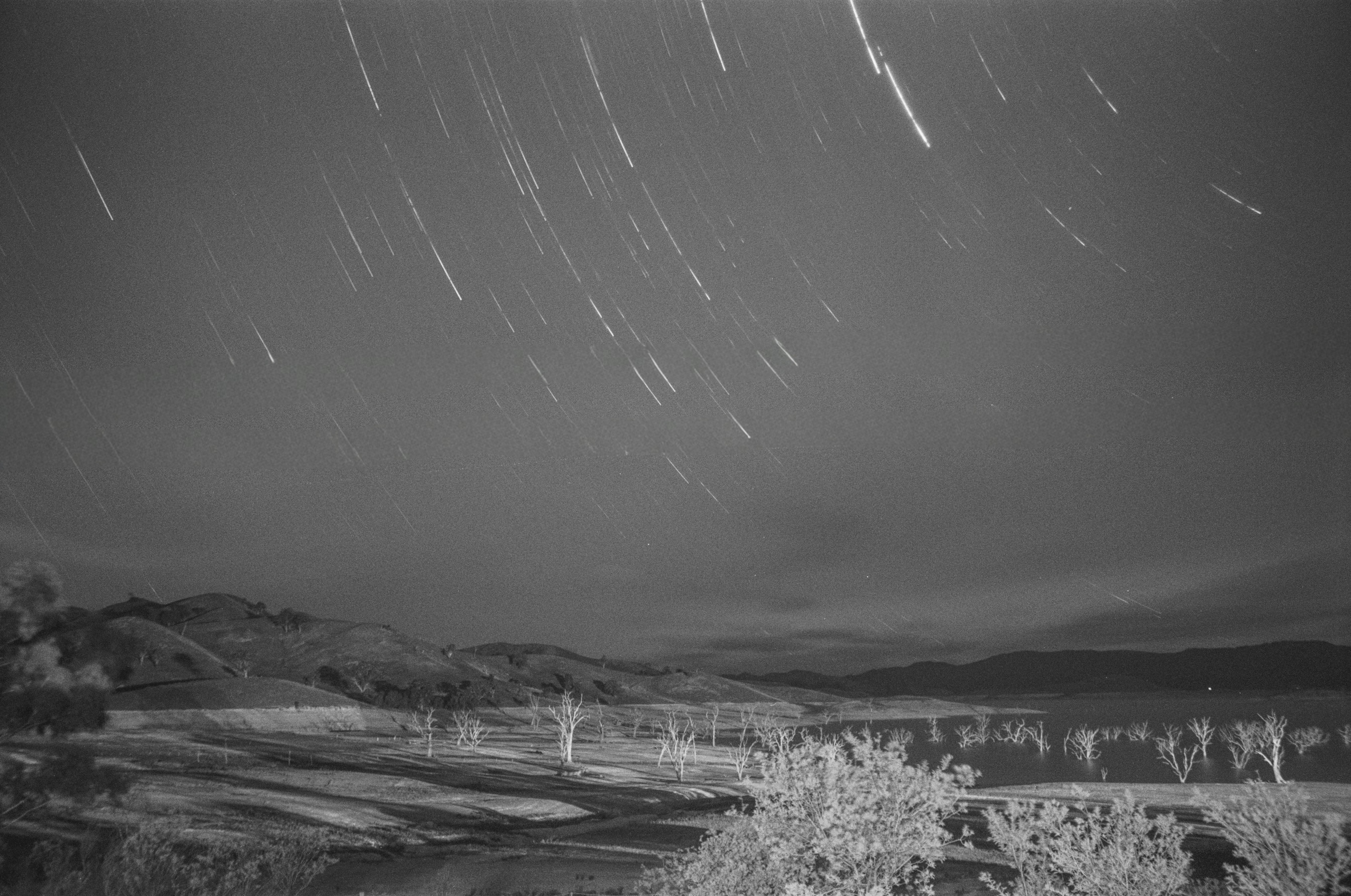 湖畔の草地と低い山並み、長時間露光の星空のような流線