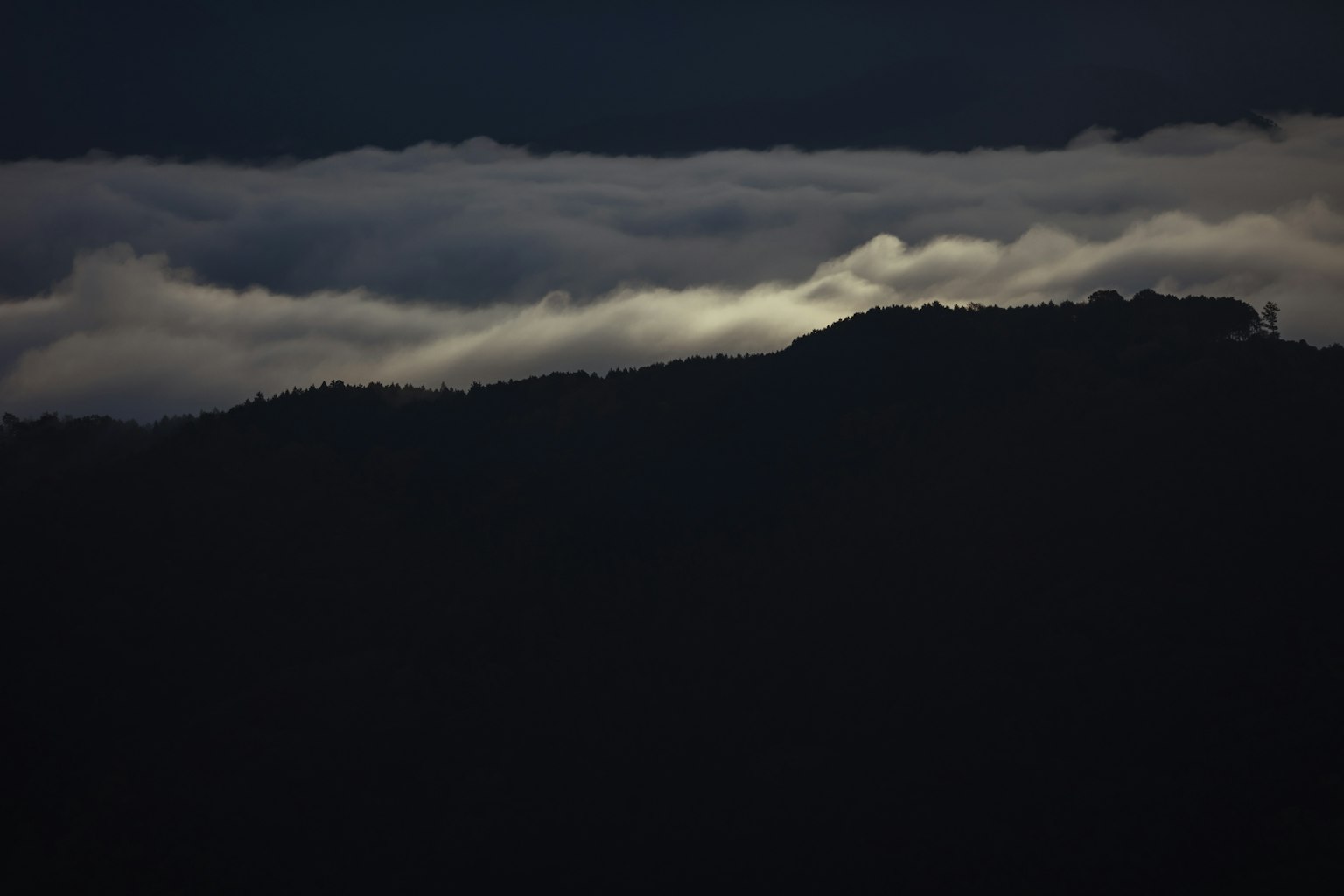 Silhouette of mountains above a layer of clouds in a dark landscape