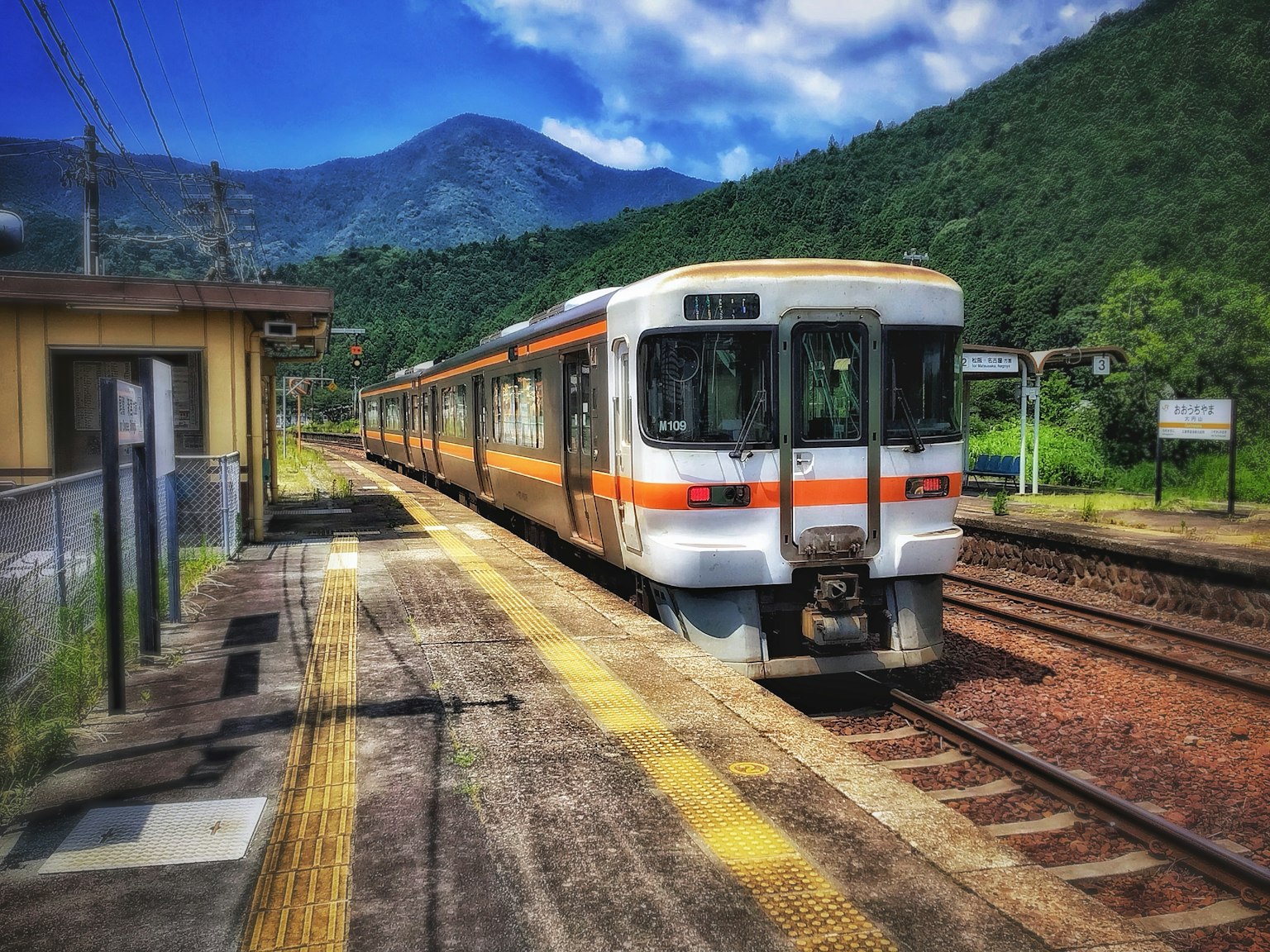Kereta api oranye dan putih di stasiun dengan latar belakang pegunungan