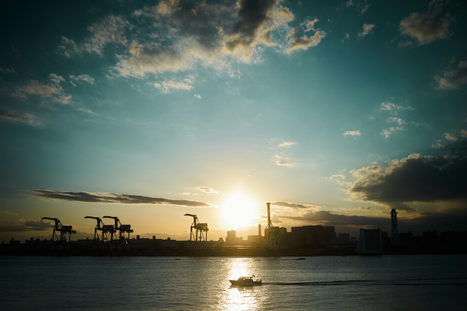Silhouette di gru contro un tramonto su acqua con skyline cittadino