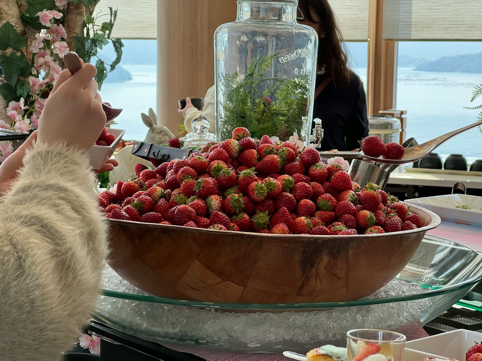 Un gran tazón lleno de fresas frescas y un recipiente de vidrio con plantas en una mesa de comedor
