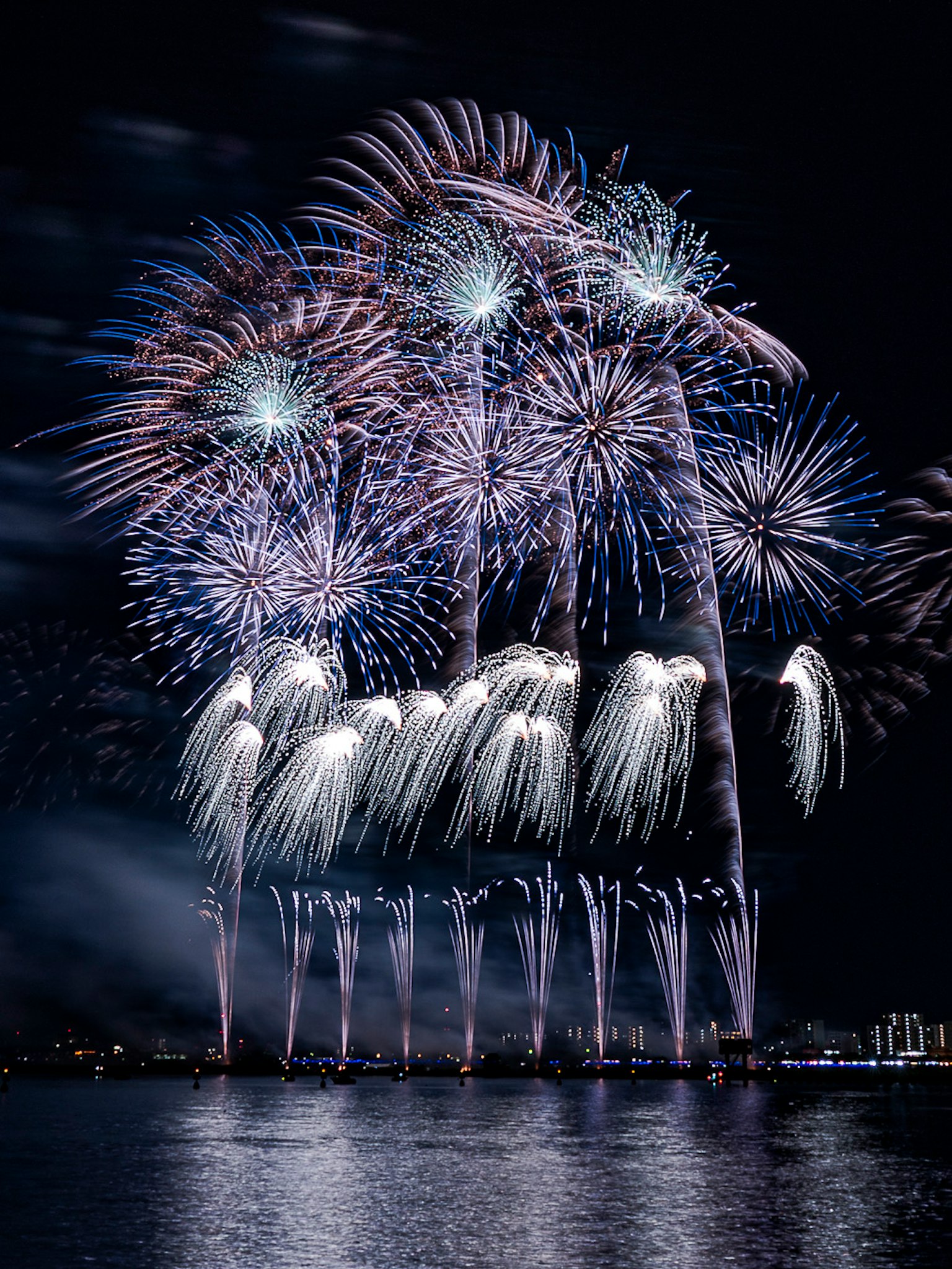 Spettacolo di fuochi d'artificio colorati che illumina il cielo notturno con riflessi sull'acqua