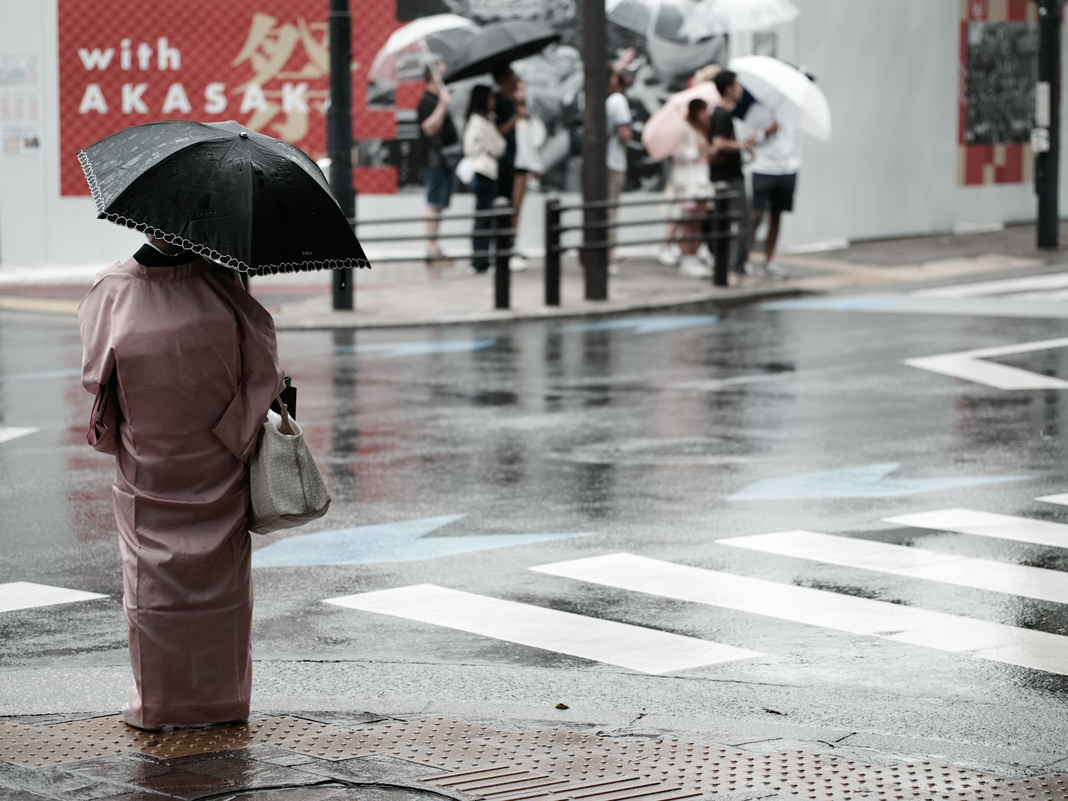 穿着和服的女性在雨中撑伞，背景有人群