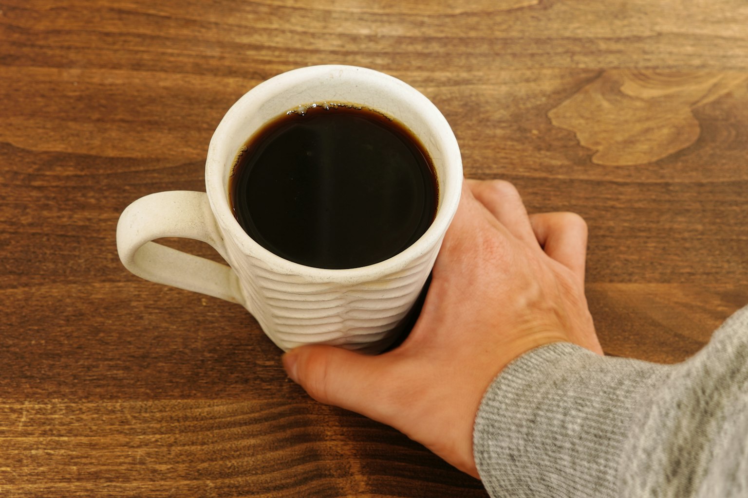 手握著咖啡杯放在木桌上