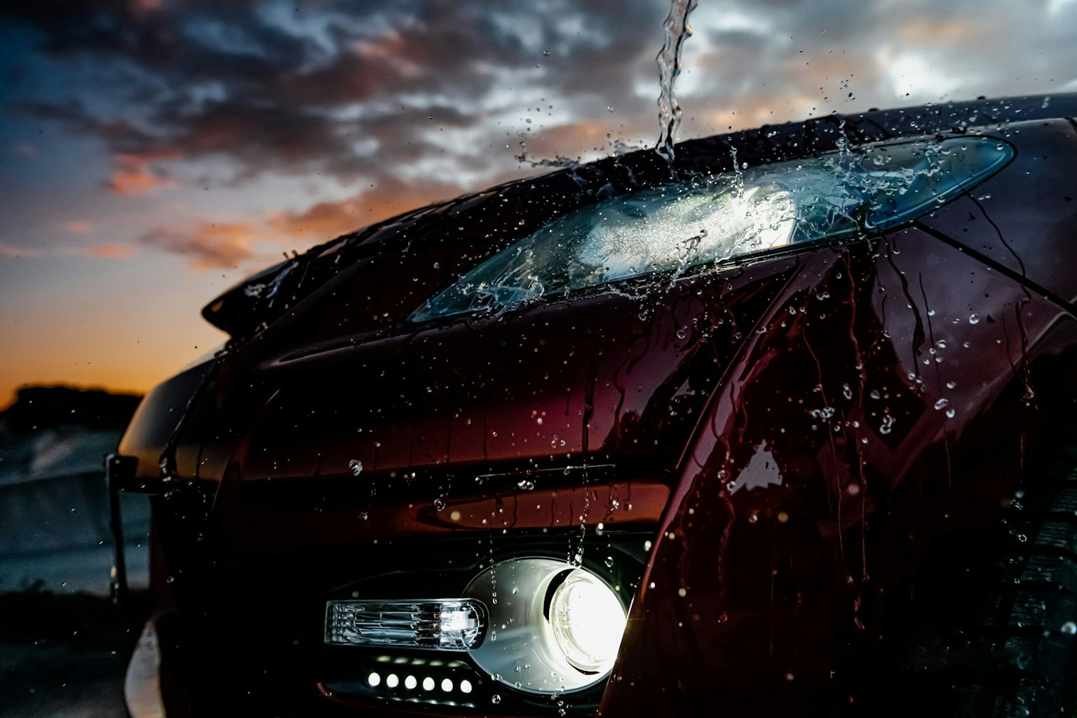 Gros plan d'une voiture rouge avec de l'eau éclaboussée sur l'avant contre un ciel de coucher de soleil
