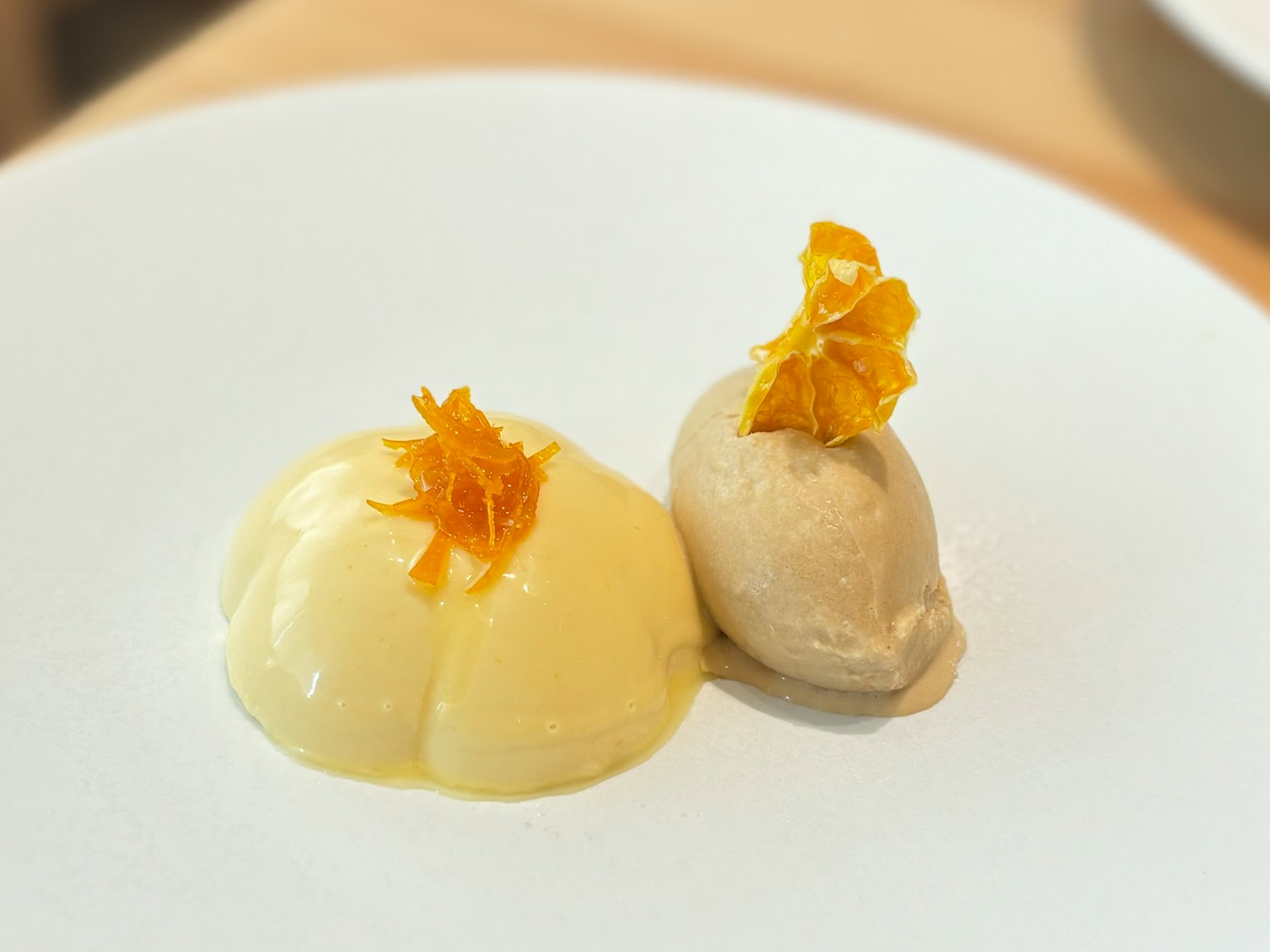 Dos postres cremosos en un plato blanco con adorno naranja en la parte superior