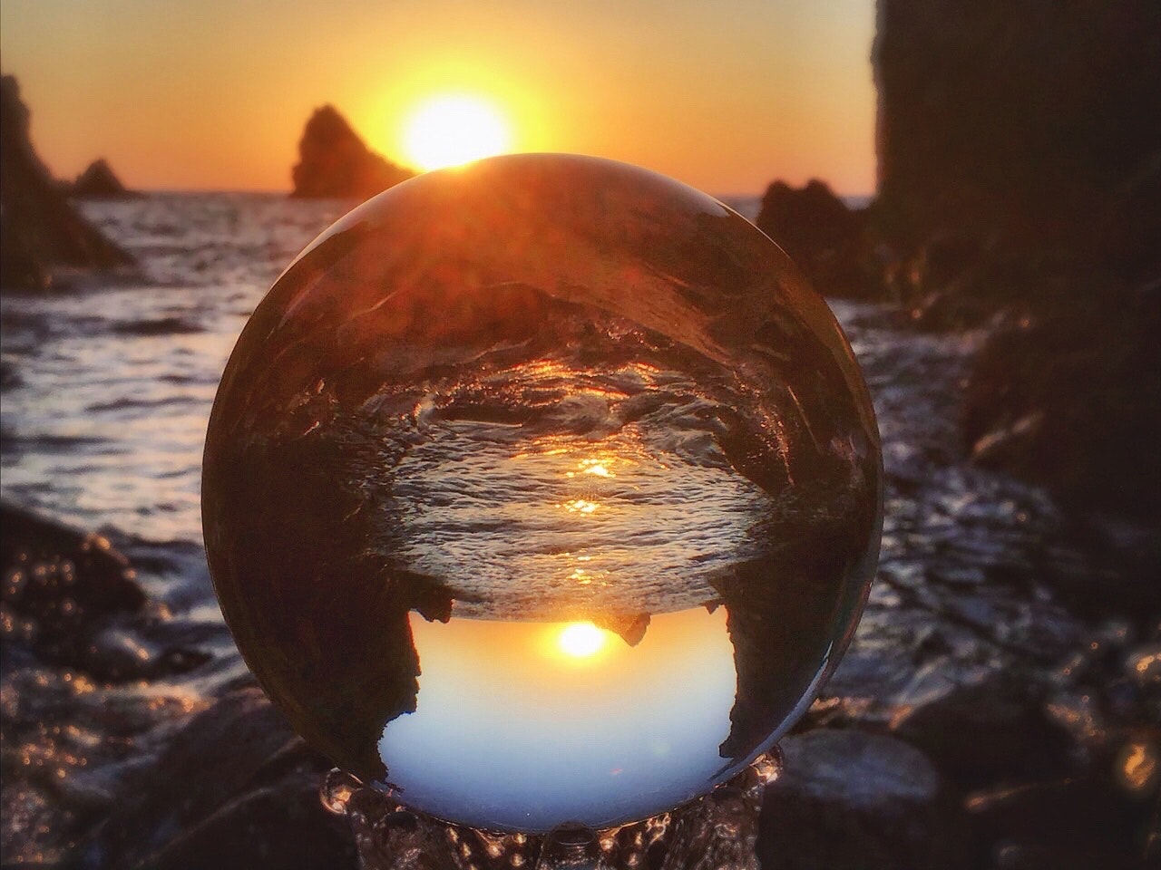 岩場に置かれたクリスタルボール越しの日本海の夕陽